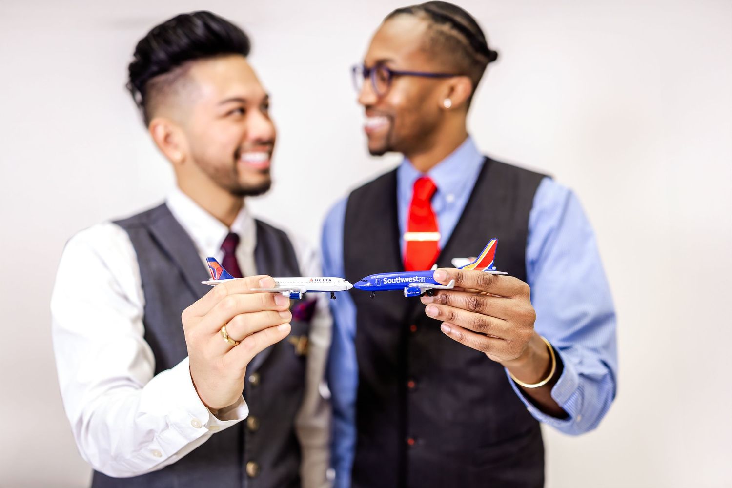 Two business professionals in formal attire playfully holding toy airplanes against white background.