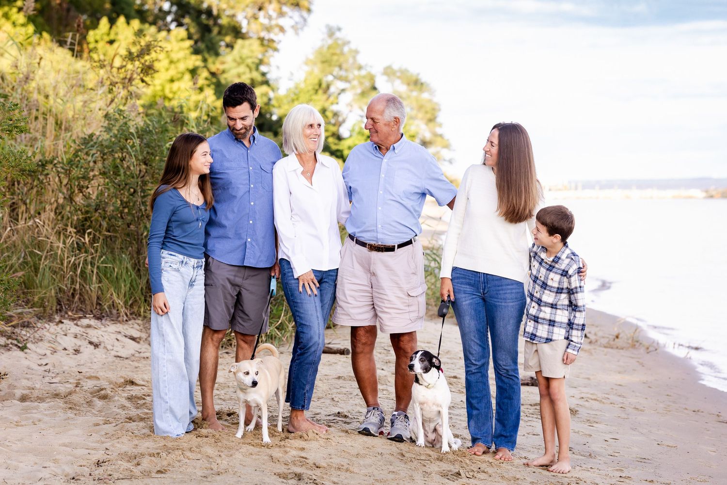 Extended family gathered for photos on a sunny beach with natural vegetation.