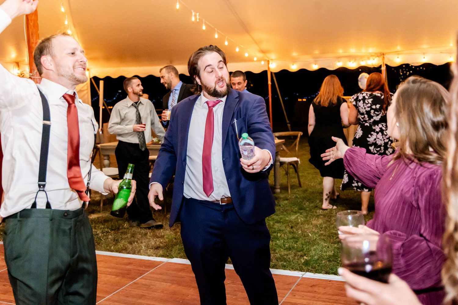 Wedding party dancing and celebrating on the dance floor under string lights at an evening reception.