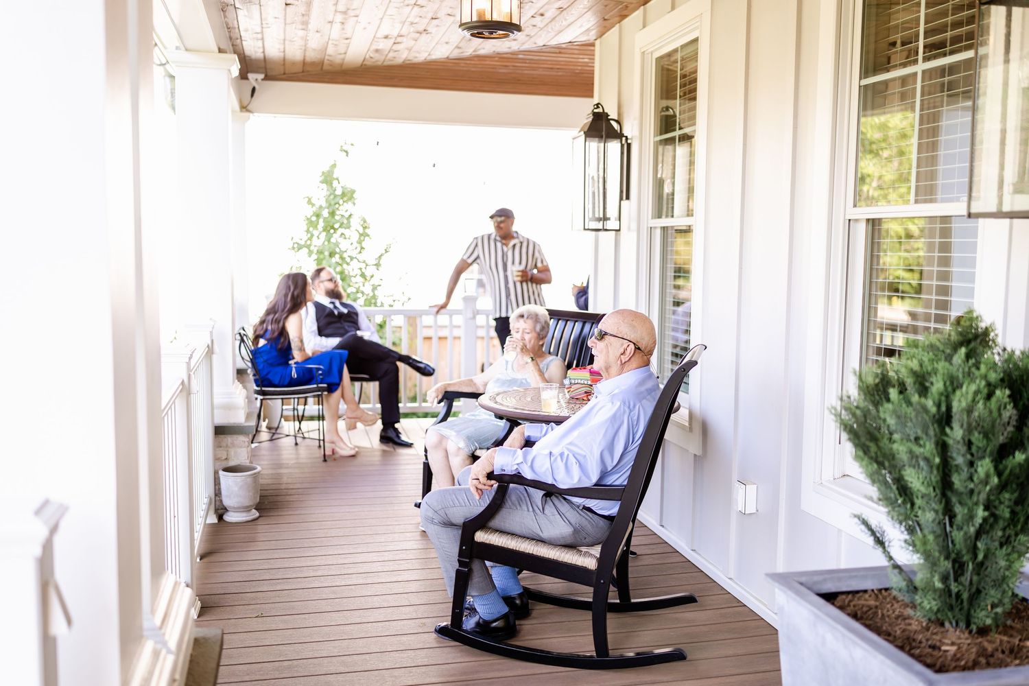 White rocking chairs lined up on a covered porch with greenery.