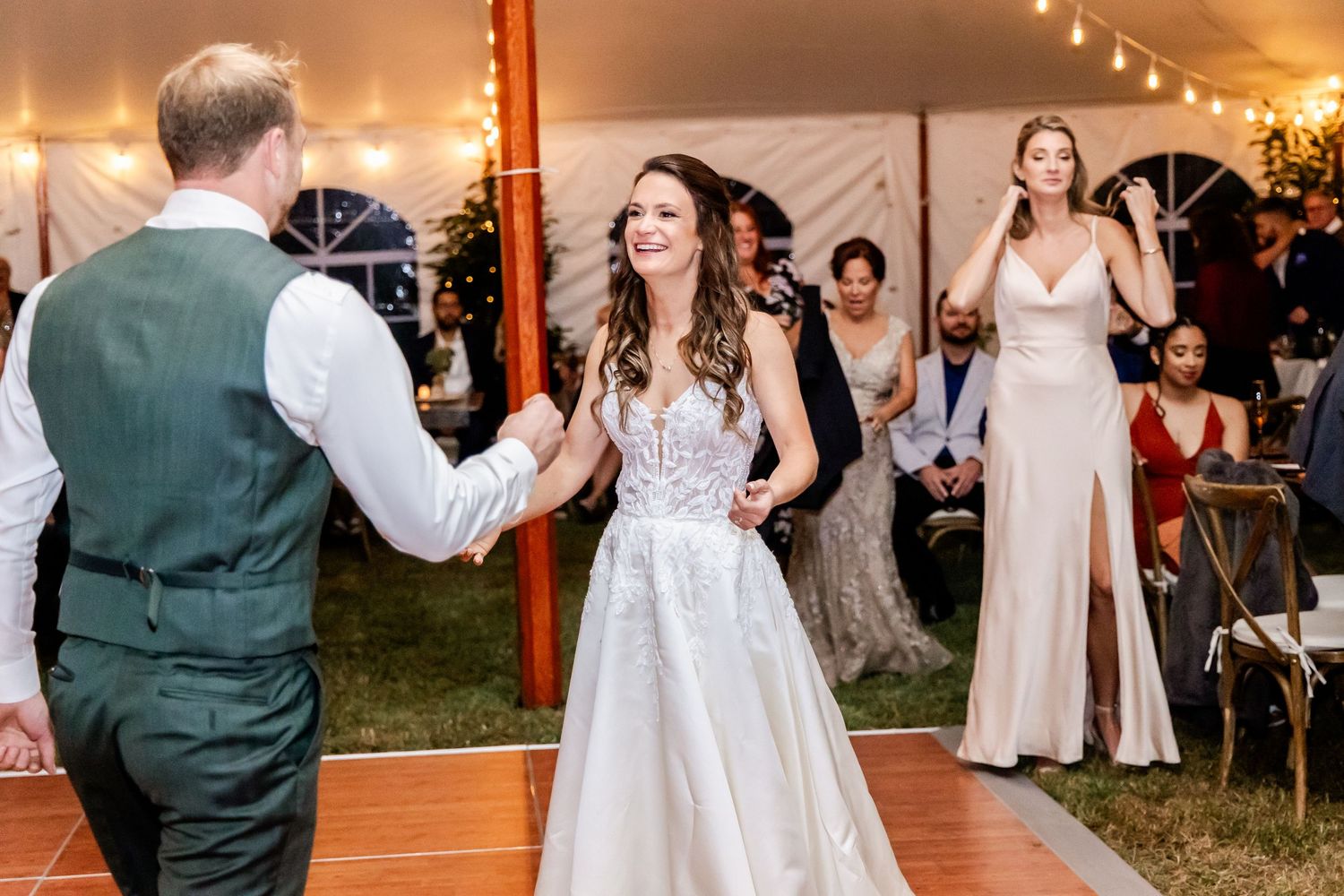 A couple shares a joyful moment while dancing at their wedding reception under string lights in a tent.
