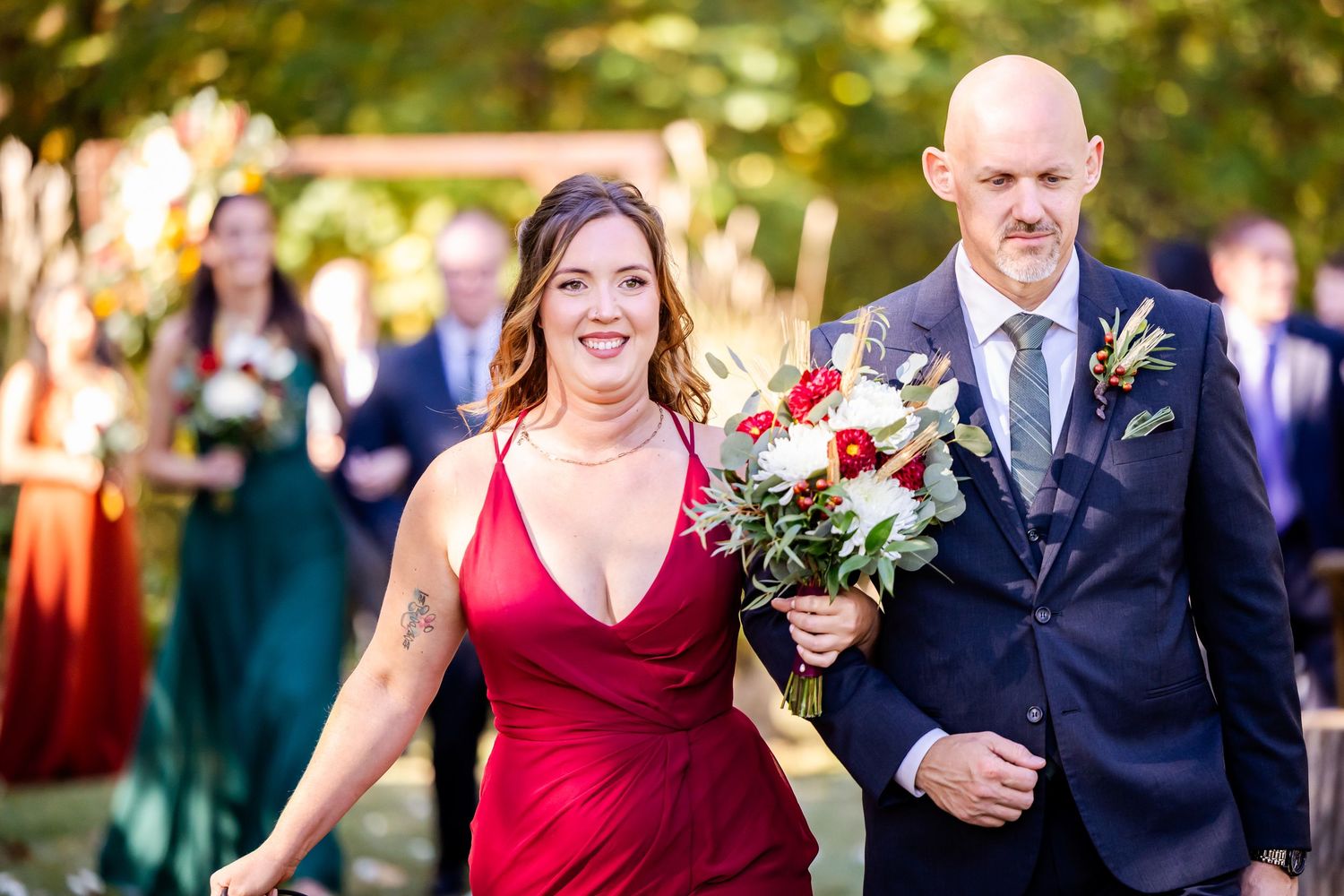 Wedding party members in burgundy dresses and navy suits walk together during an outdoor celebration.