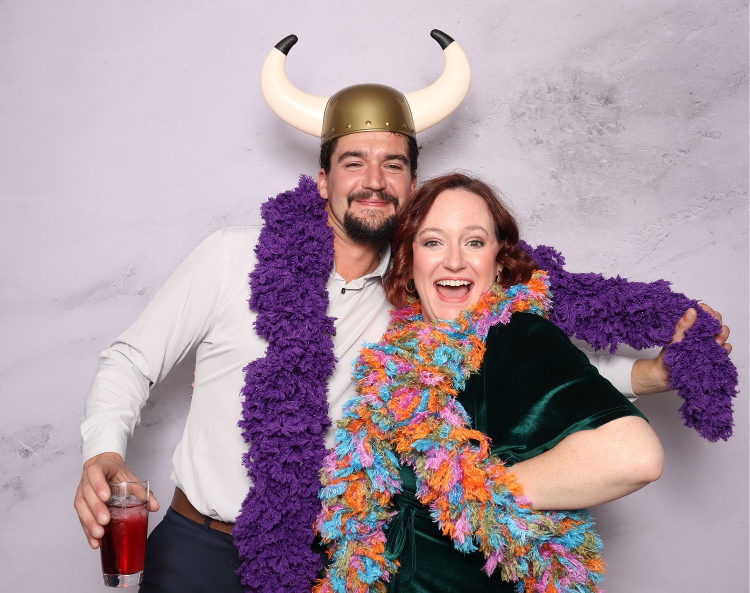 Couple in viking hat and colorful boas posing playfully at a party photo booth.