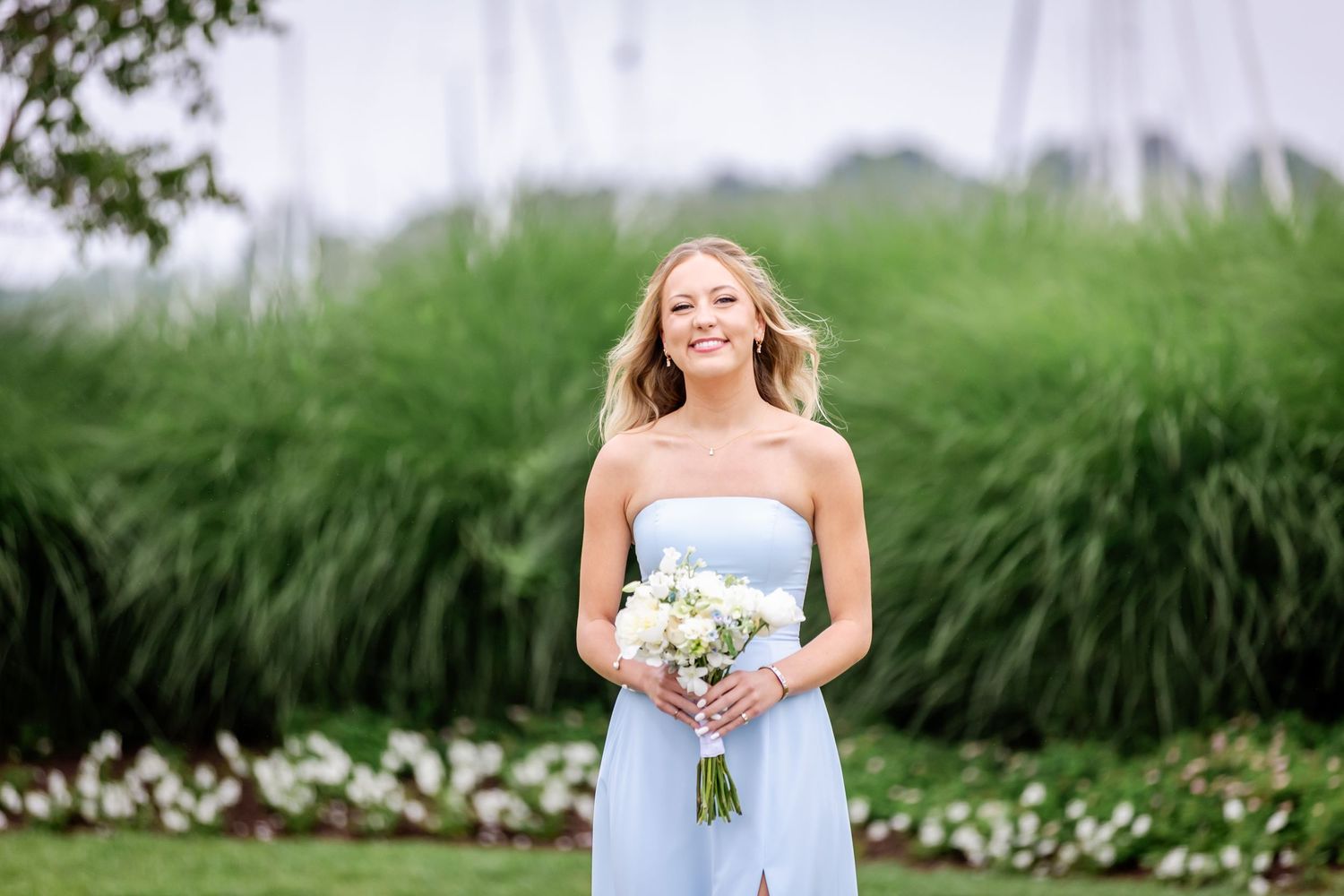 Bridesmaids in light blue dresses hold bouquets while standing in a grassy field.