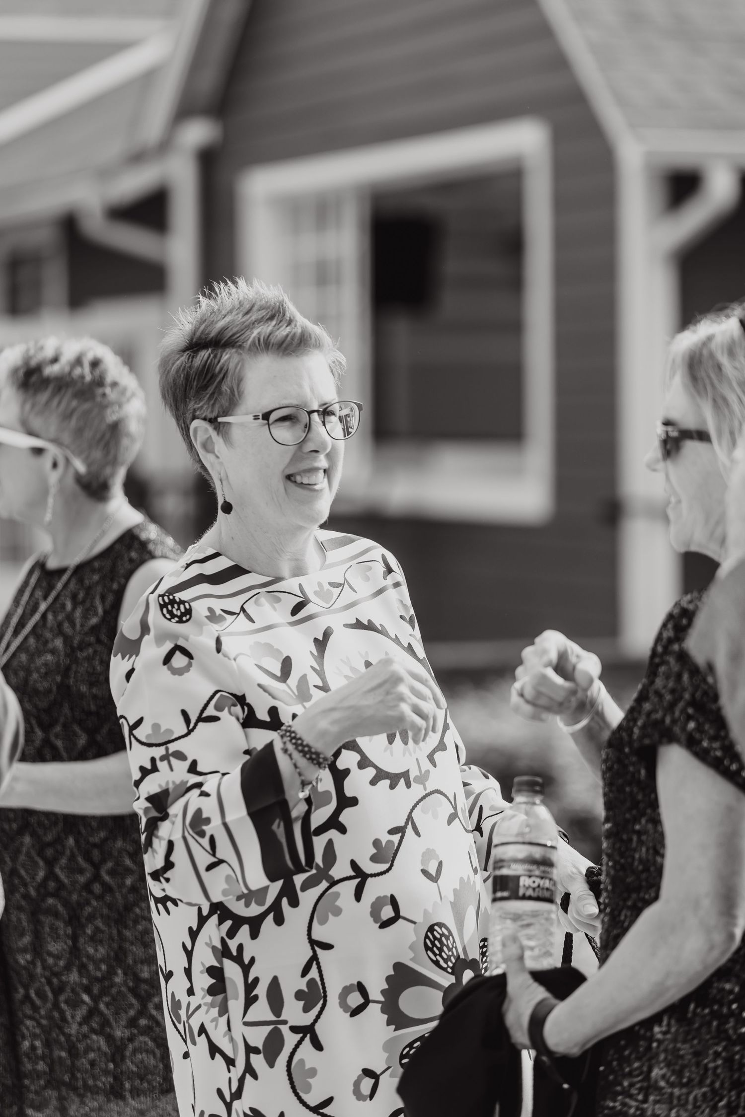 Group of wedding guests in black and white patterned dresses enjoying drinks and conversation outdoors.
