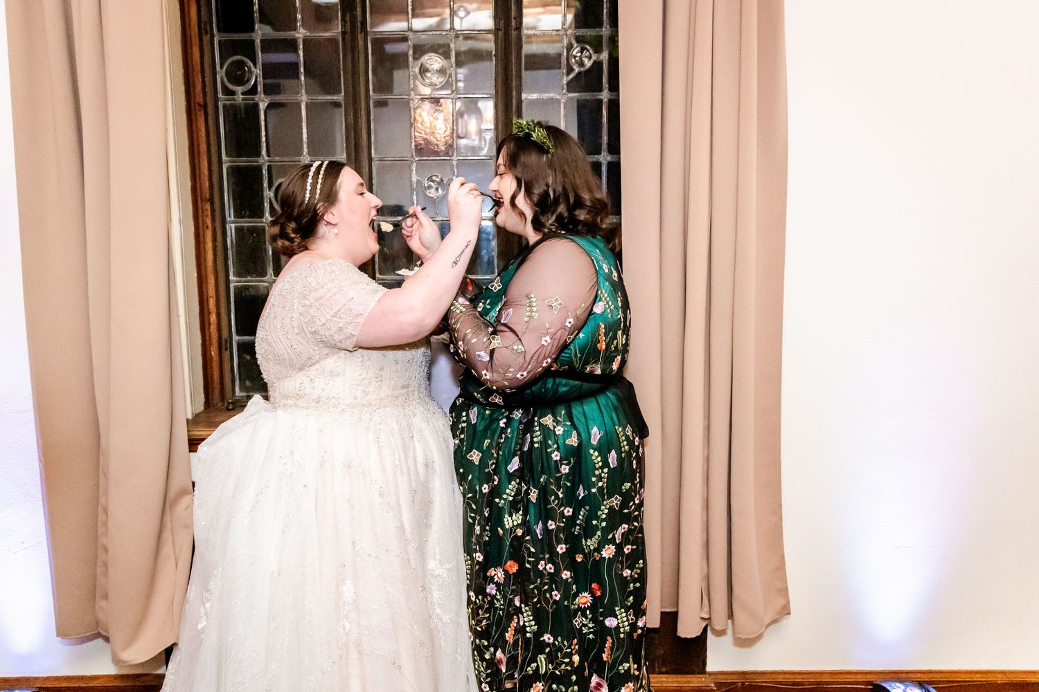 Two wedding guests share a celebratory moment in an indoor venue.