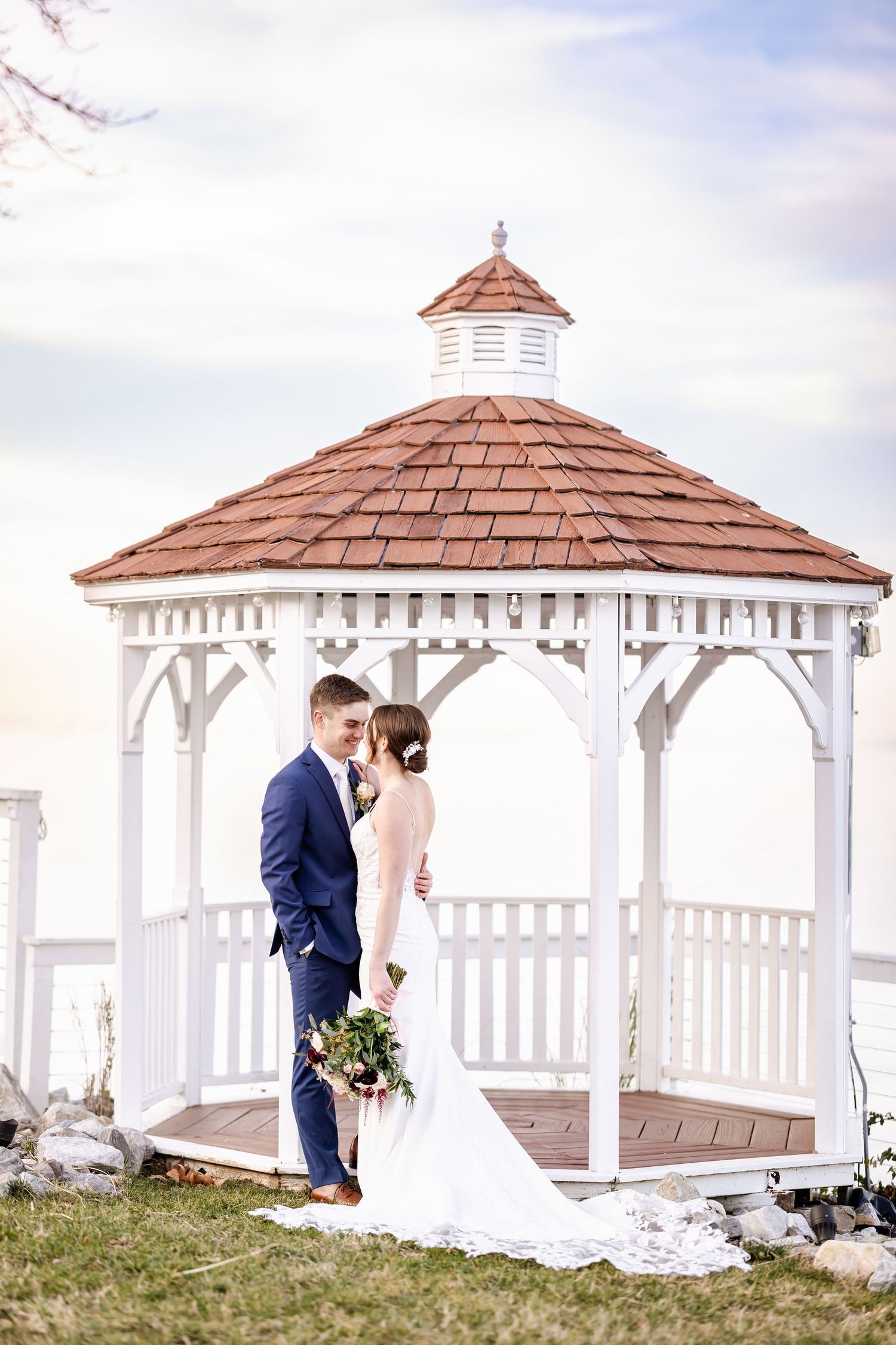 Wedding couple shares intimate moment under white gazebos with brown shingled roofs.