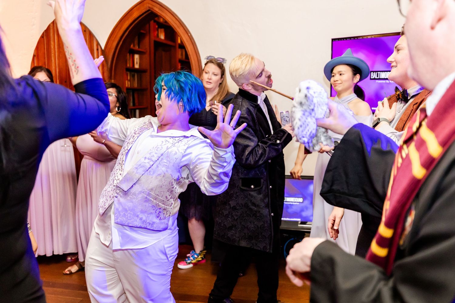 Energetic dance moves at a party with gothic arched windows and decorative lighting in the background.