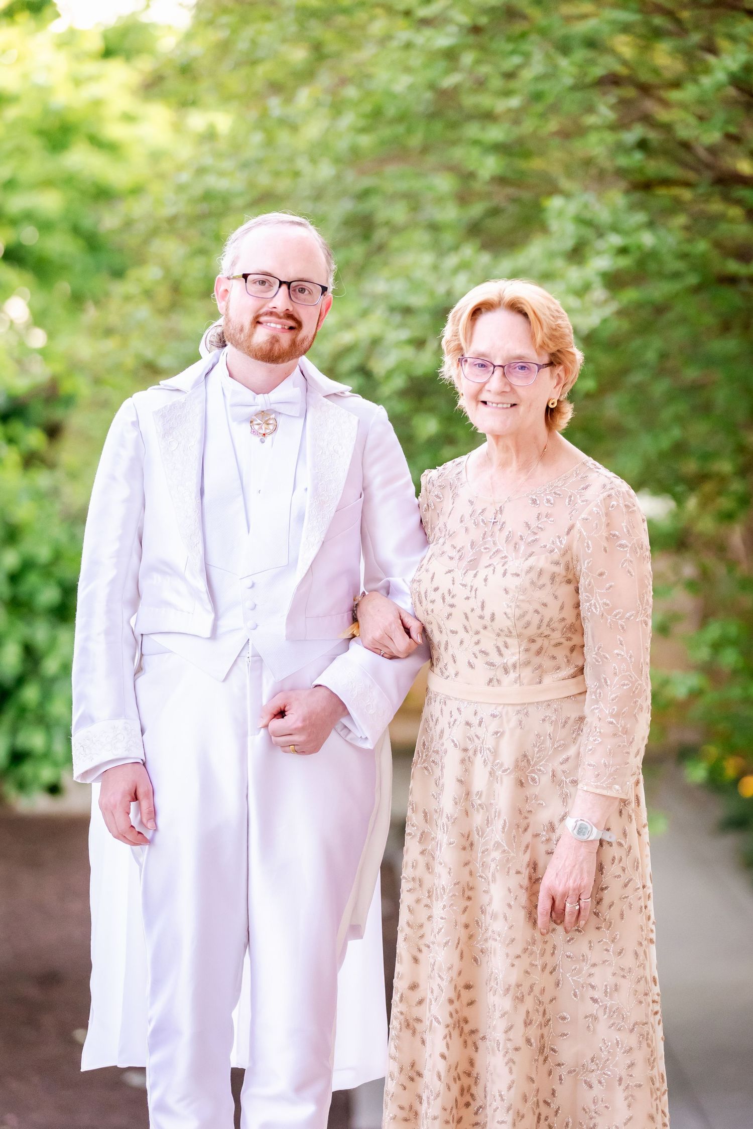 Two wedding party members pose together, one in all white and one in a champagne lace dress.