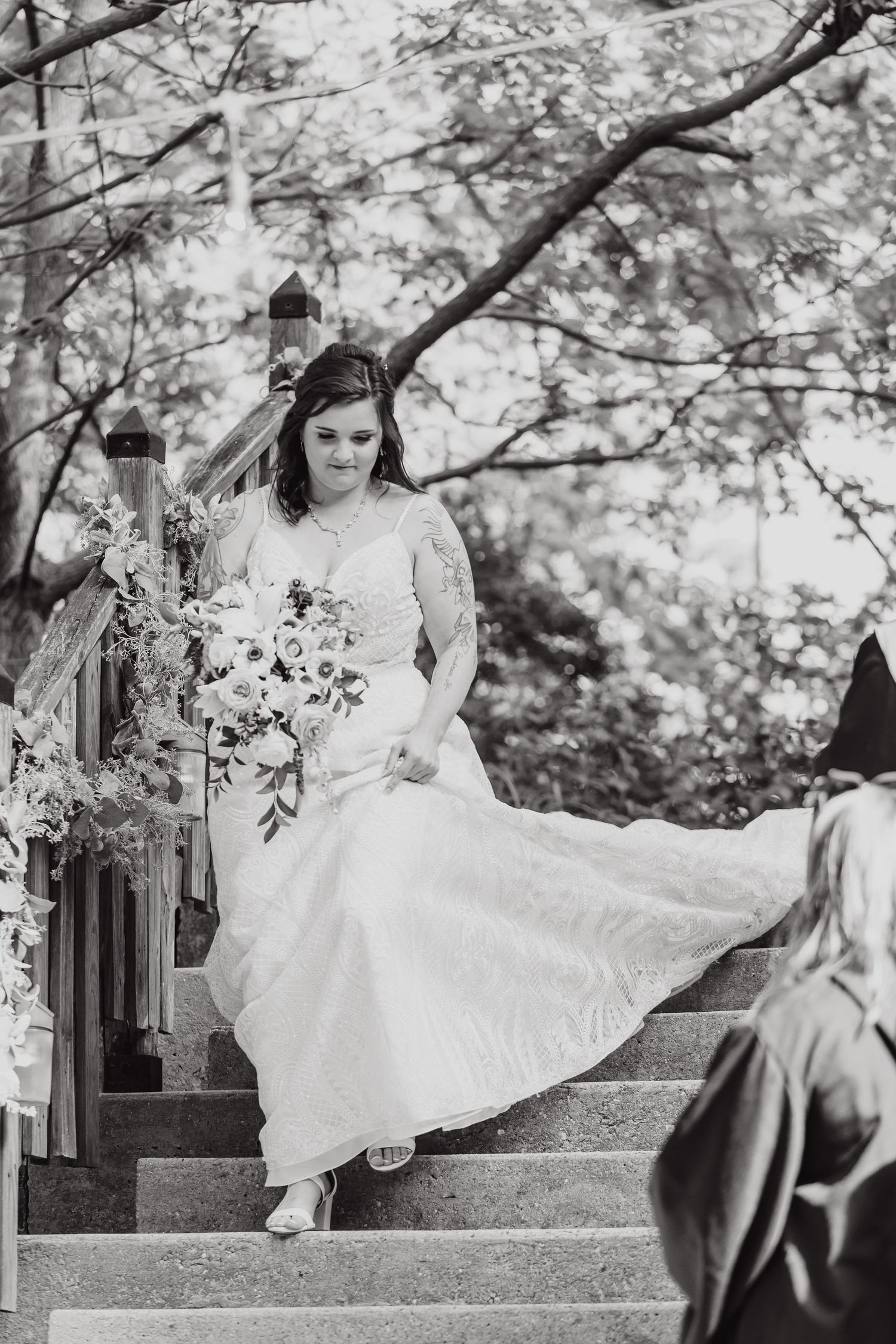 Black and white photo of bride descending stone stairs decorated with floral arrangements.