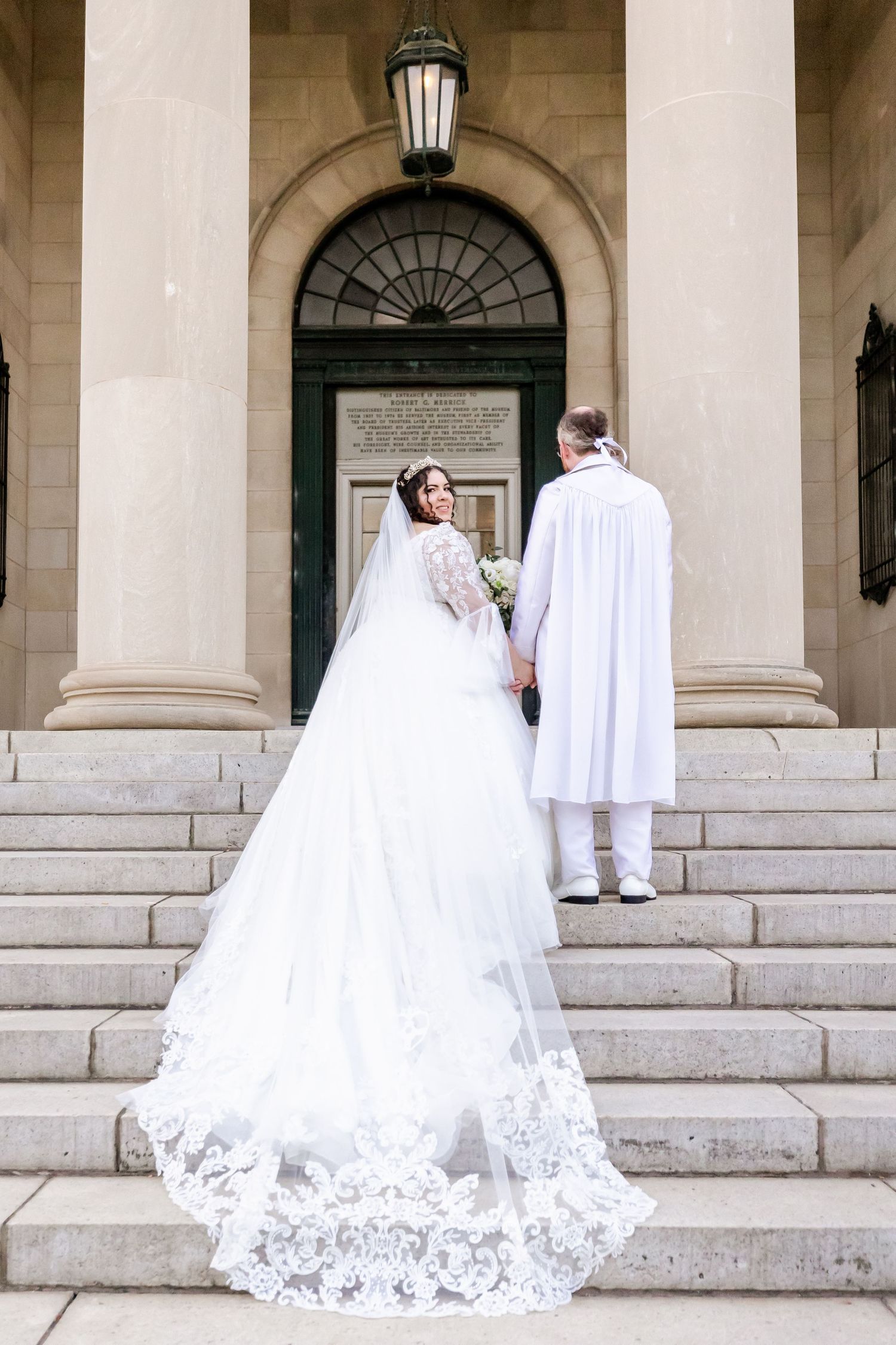 Stunning lace wedding dress train displayed on marble steps of historic building entrance.
