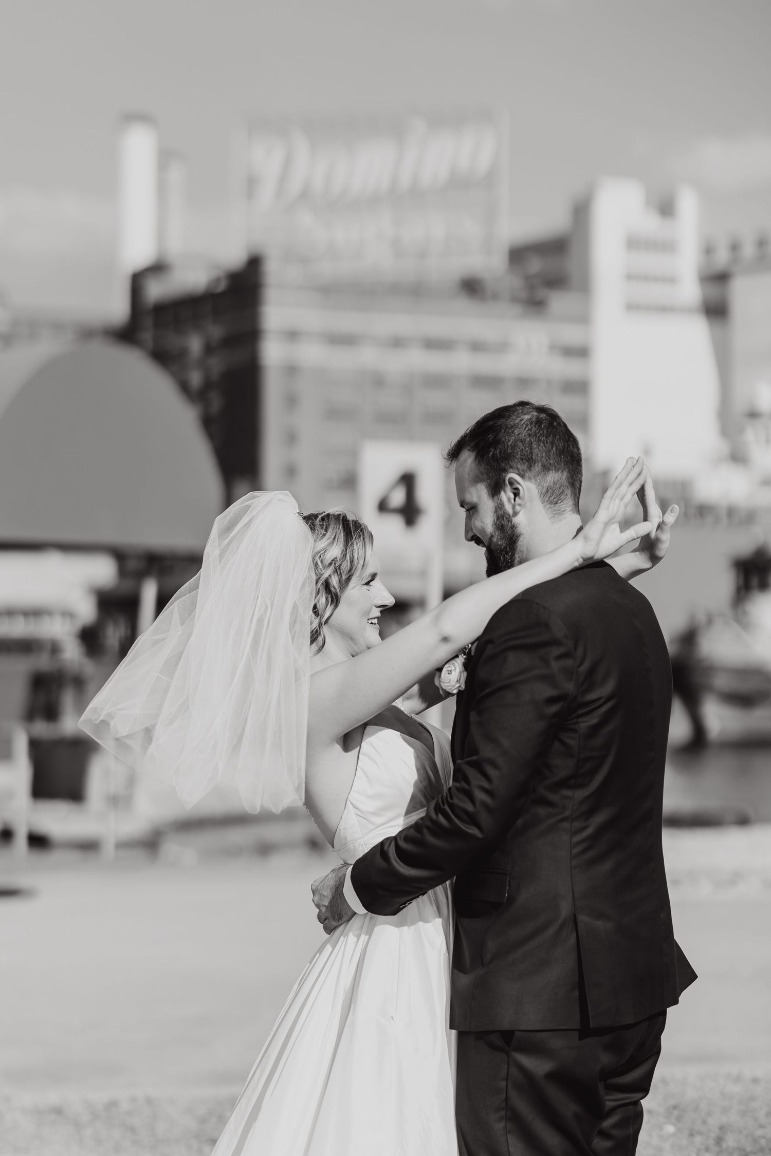 A bride and groom share an intimate moment outdoors in black and white, with urban buildings visible in the background.