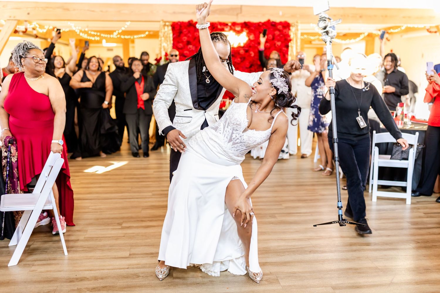 Couple performs dramatic dance dip during wedding reception with red backdrop and guests watching.