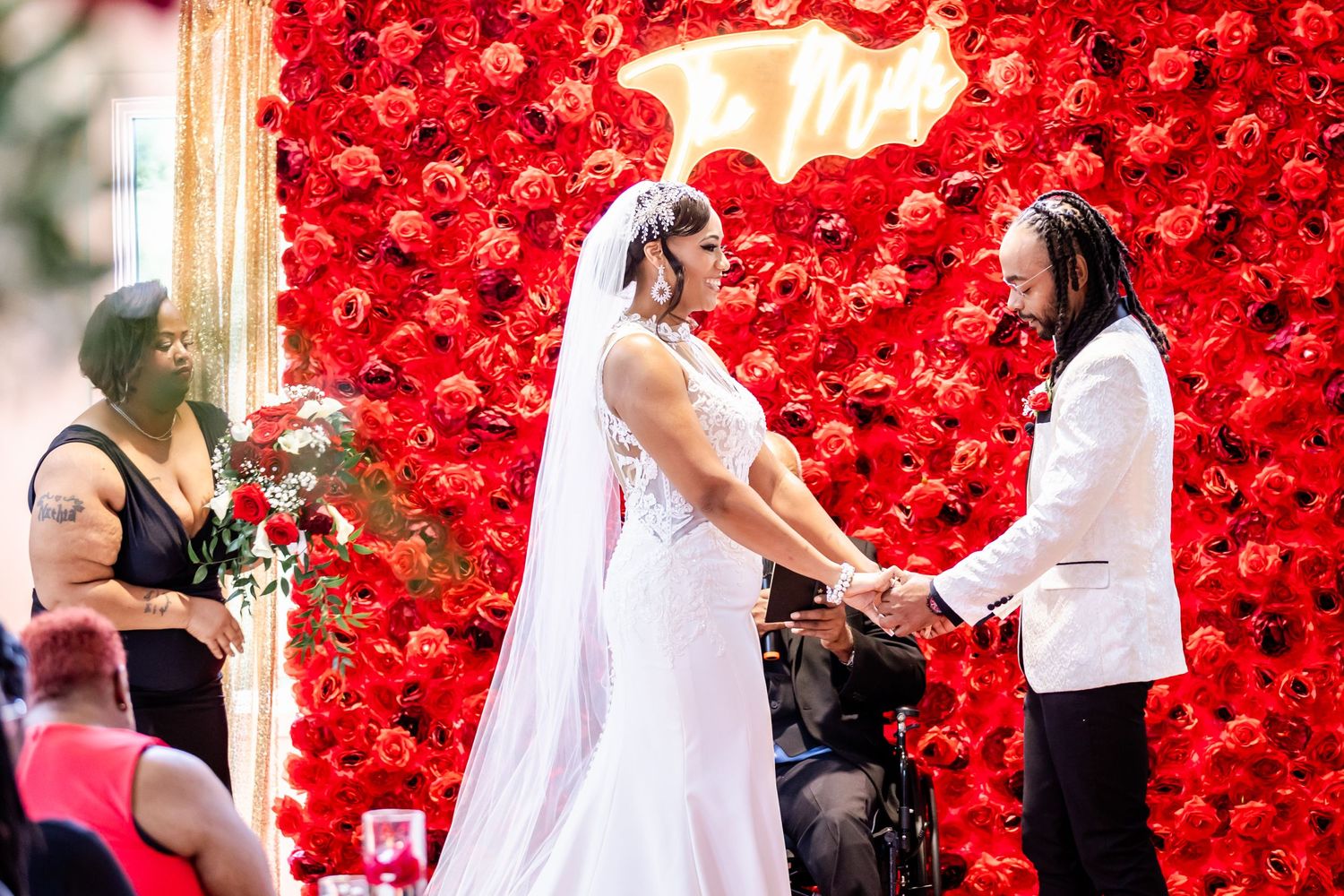 Wedding ceremony in front of stunning red rose wall backdrop.