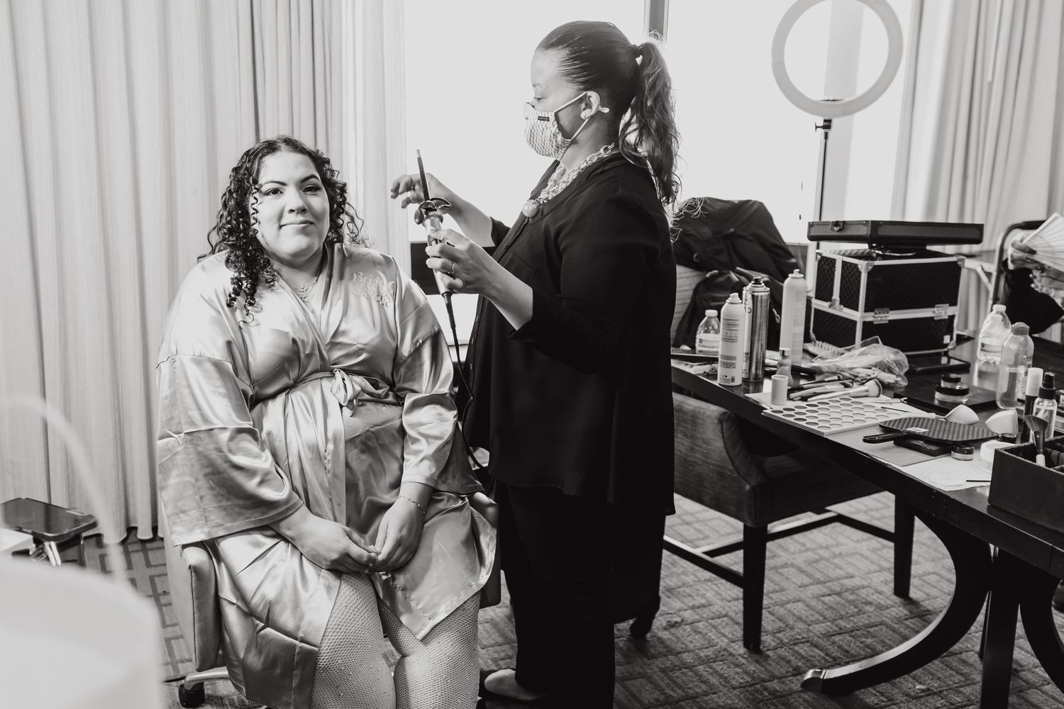 Black and white photo of wedding preparation moment with hair and makeup styling.