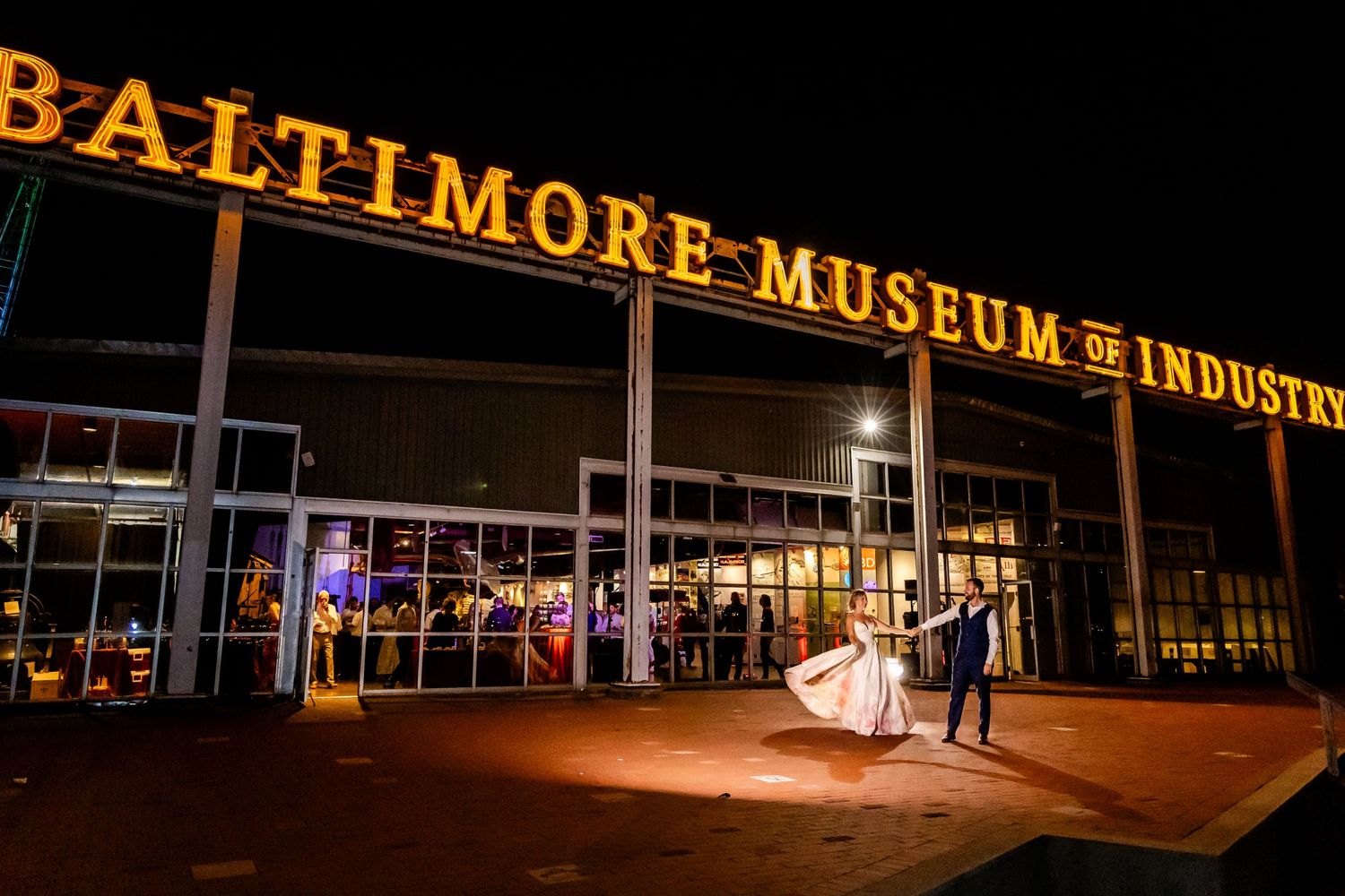 Illuminated Baltimore Museum of Industry sign at night with couple posing in front.