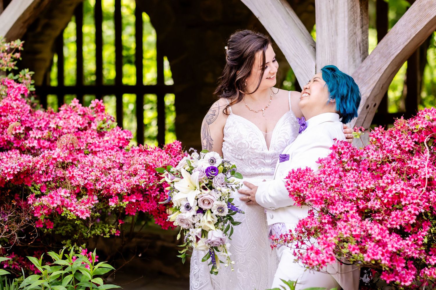 A romantic wedding portrait framed by bright pink azalea blooms under a wooden structure.