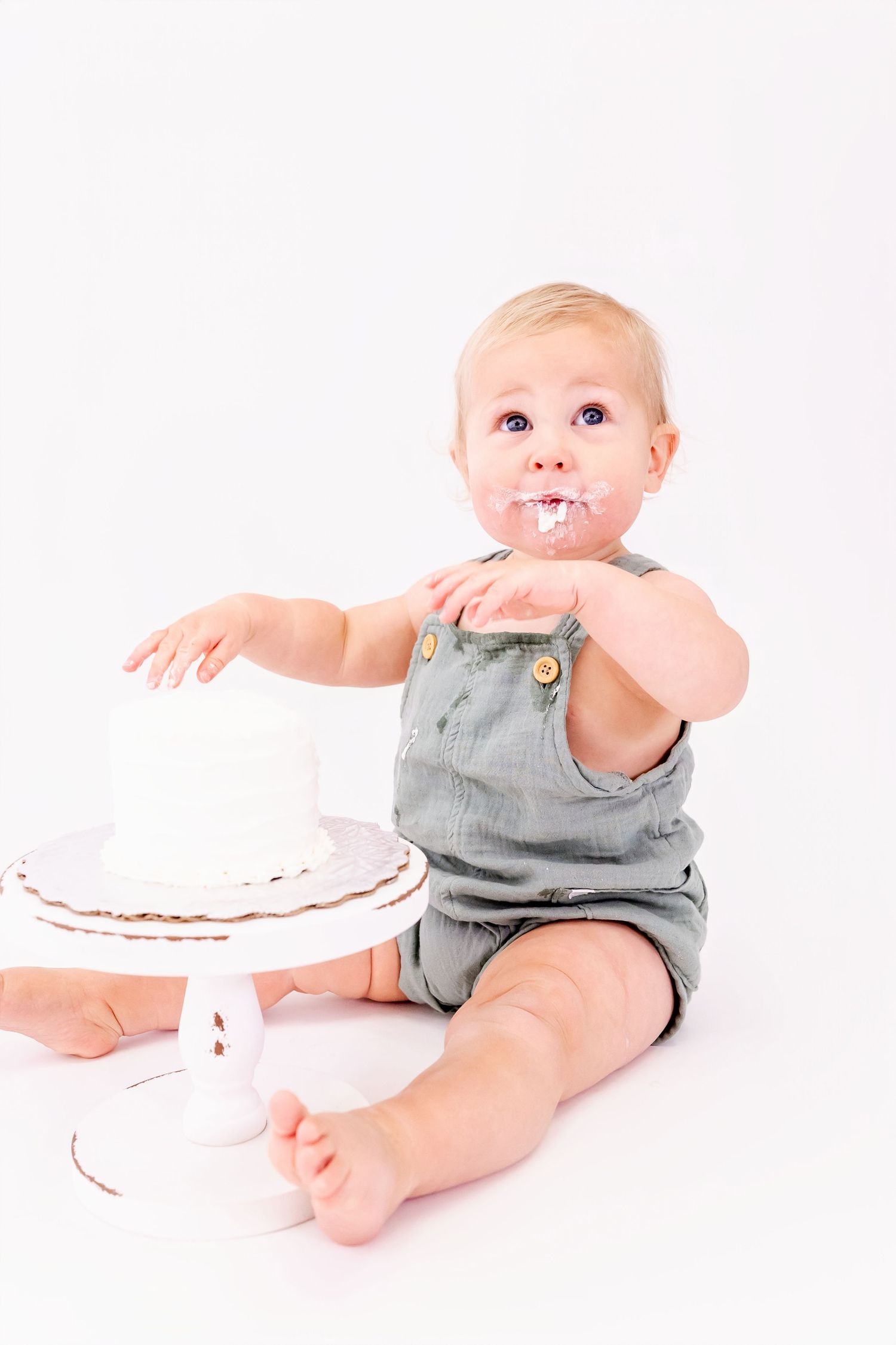 Baby in gray outfit playing with white cake during studio photoshoot.