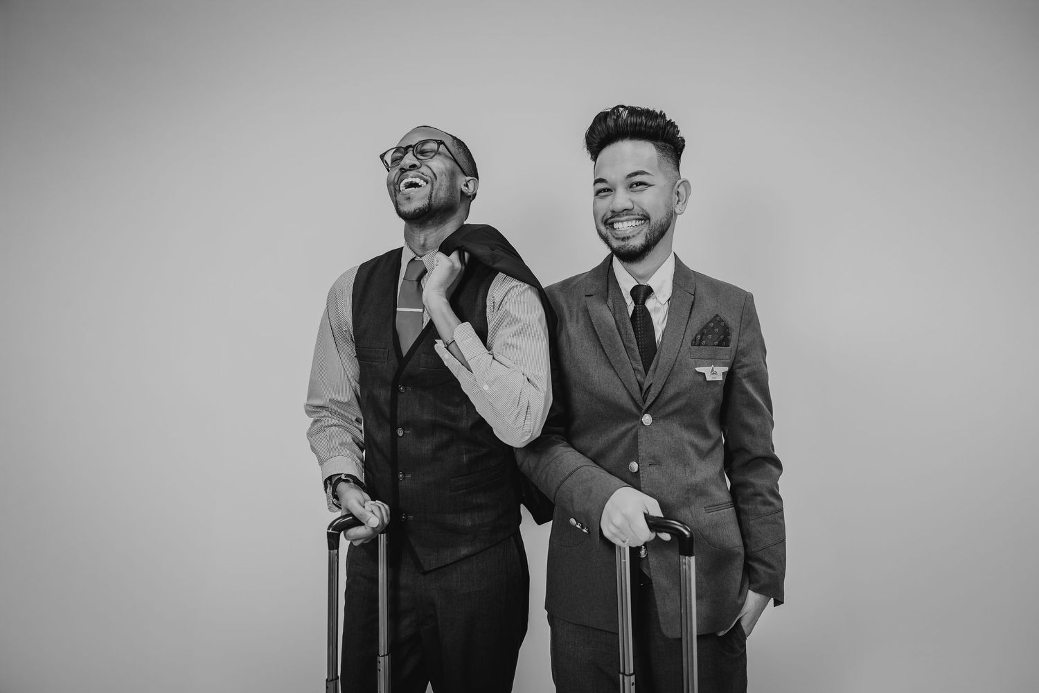 Two stylishly dressed men in suits laugh together while holding canes in black and white photography.