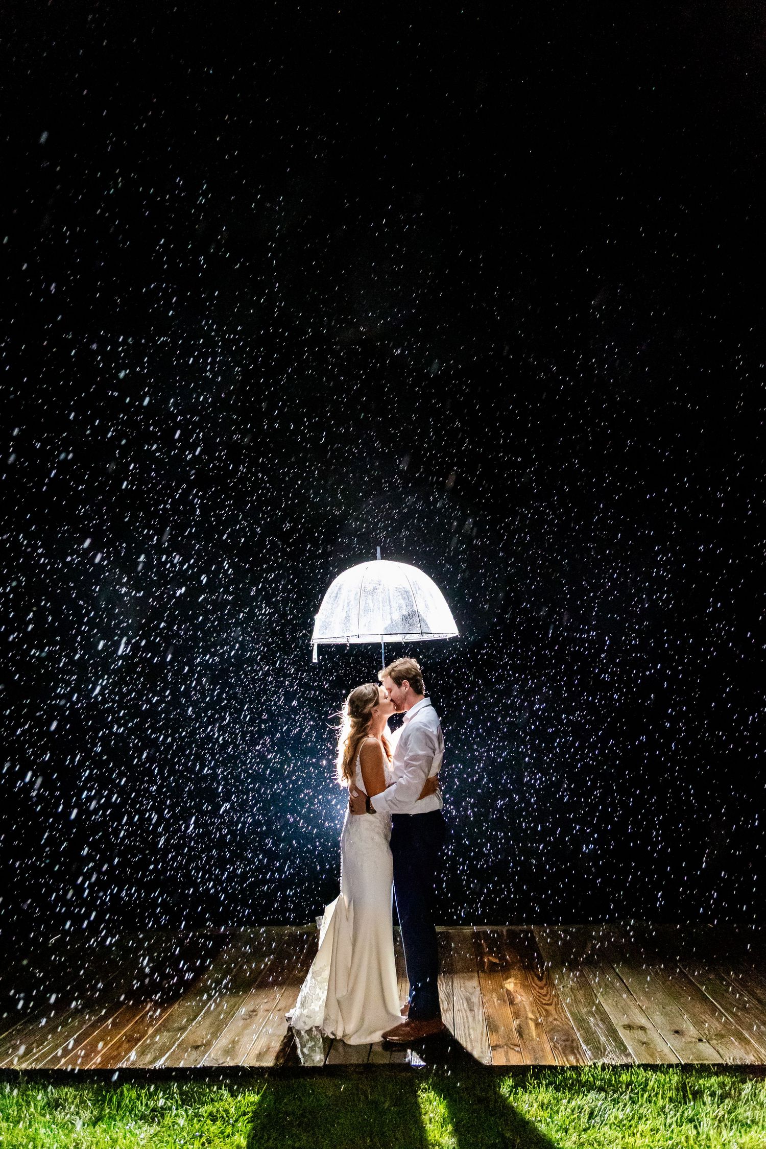 A couple shares a romantic moment under an umbrella in the rain at night with dramatic lighting.