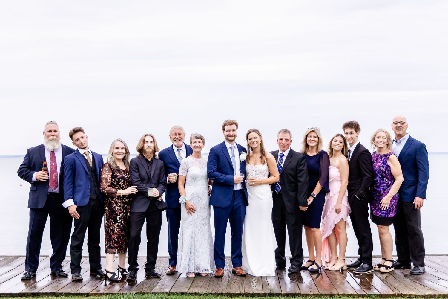 Large wedding party group photo with everyone lined up on a wooden boardwalk.