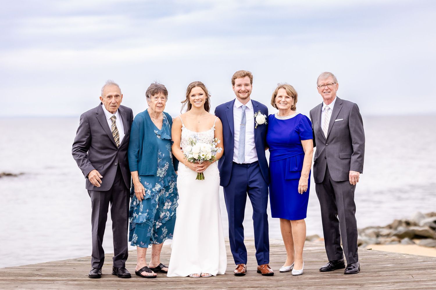 A group poses together for formal portraits along a scenic beach boardwalk.