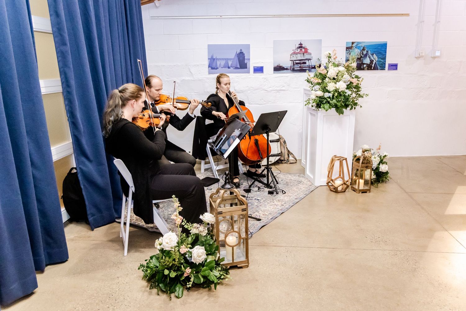 String quartet performing at an elegant wedding ceremony with floral arrangements and blue drape backdrop.
