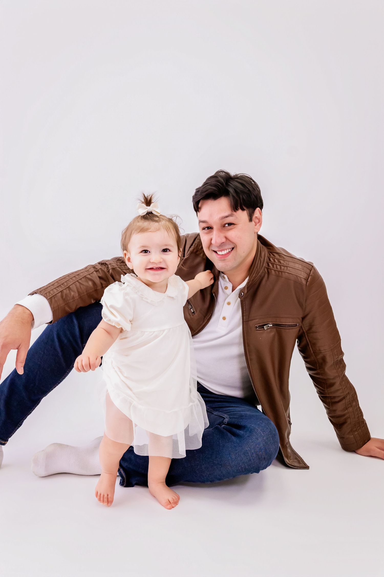 A series of four studio portraits showing a parent and child in white and brown outfits lying on a white background.