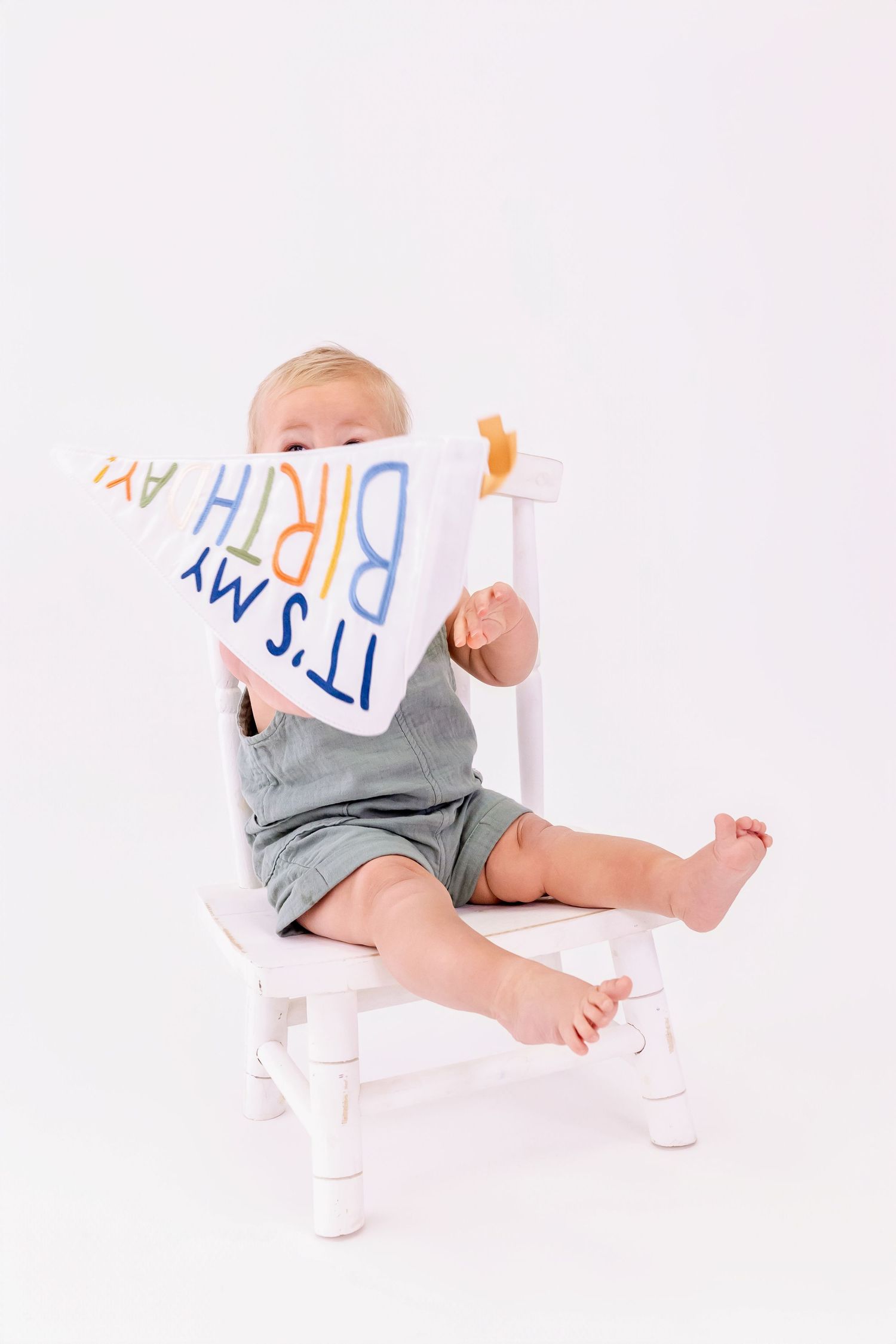 Baby in gray outfit playing with white letters on white background.
