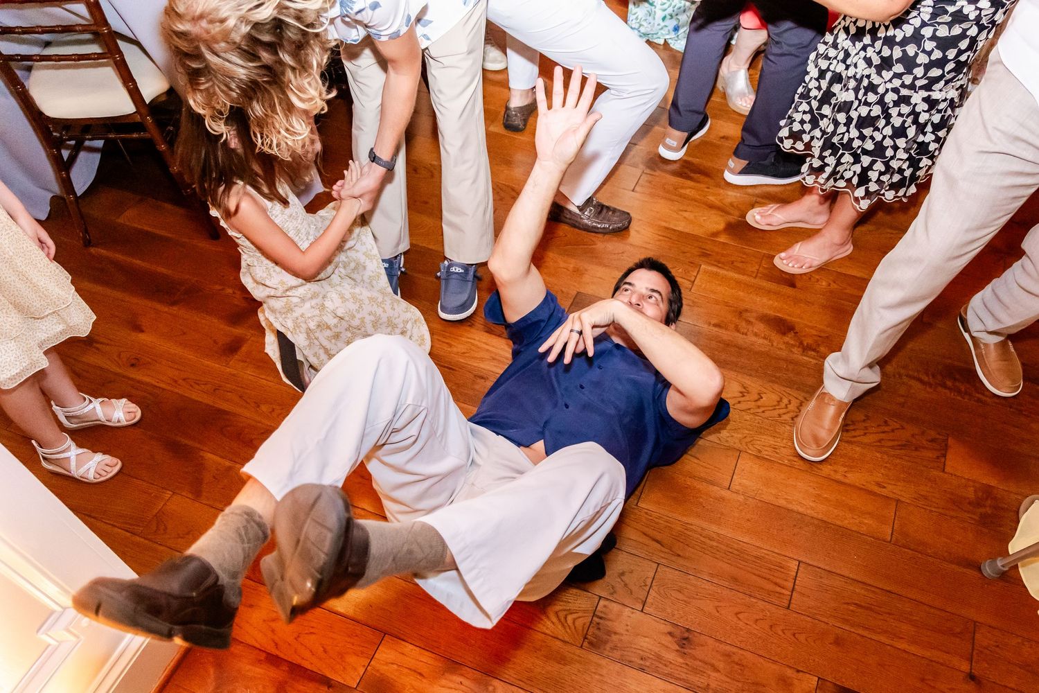 A couple dances together on a wooden floor surrounded by other people at what appears to be a wedding reception.
