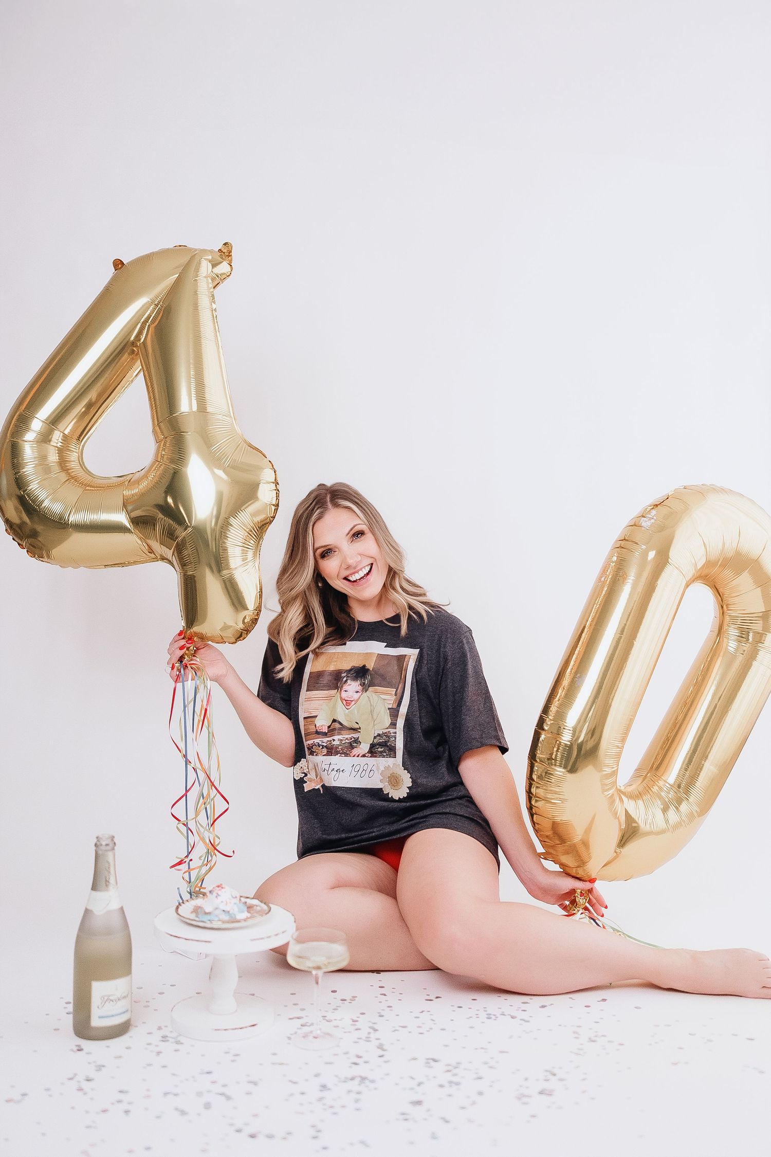 Woman in casual black shirt lying on floor with gold number 40 balloons and confetti for birthday photoshoot.