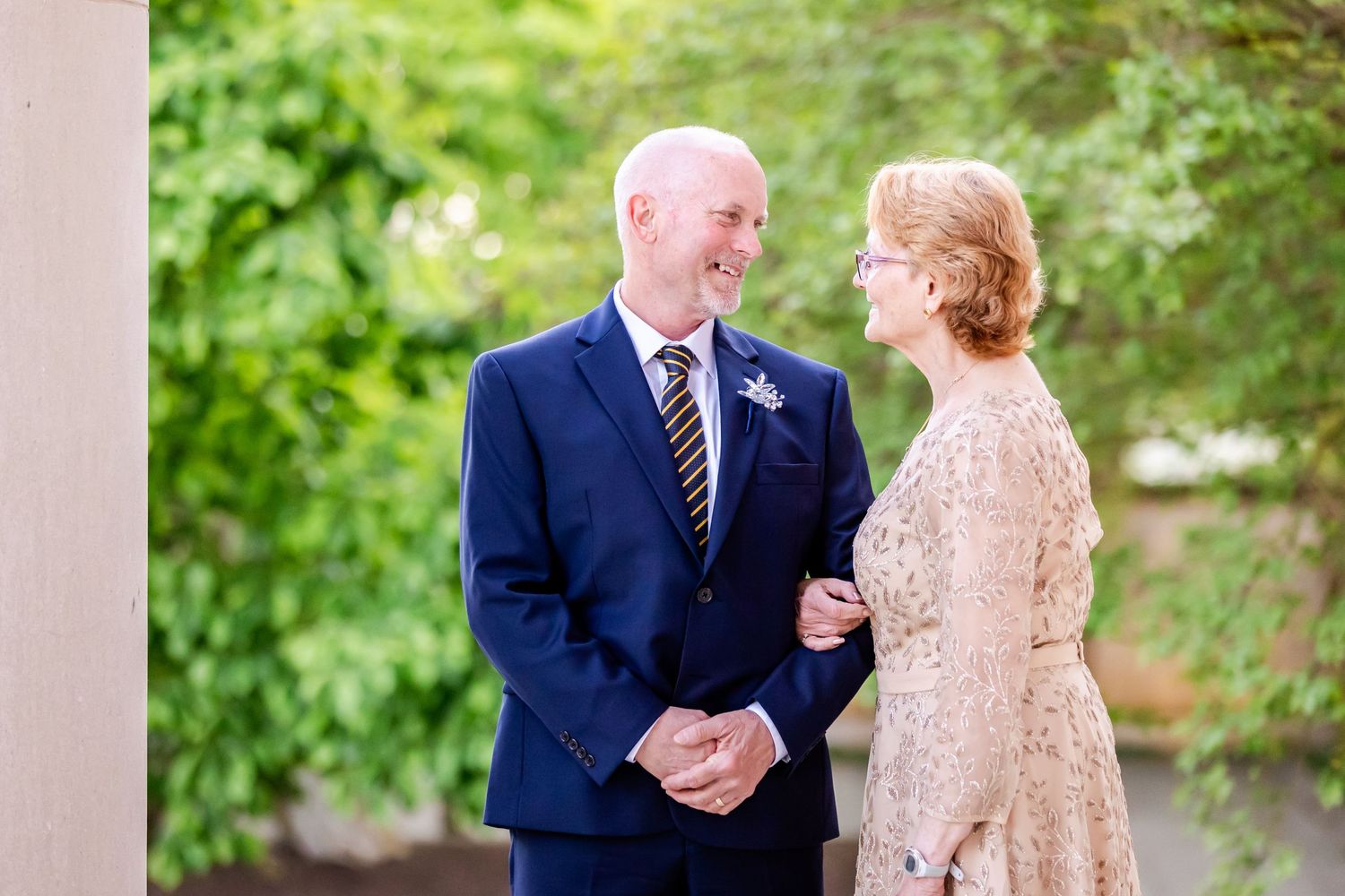 A couple shares a tender moment while dressed in formal attire against a green outdoor background.