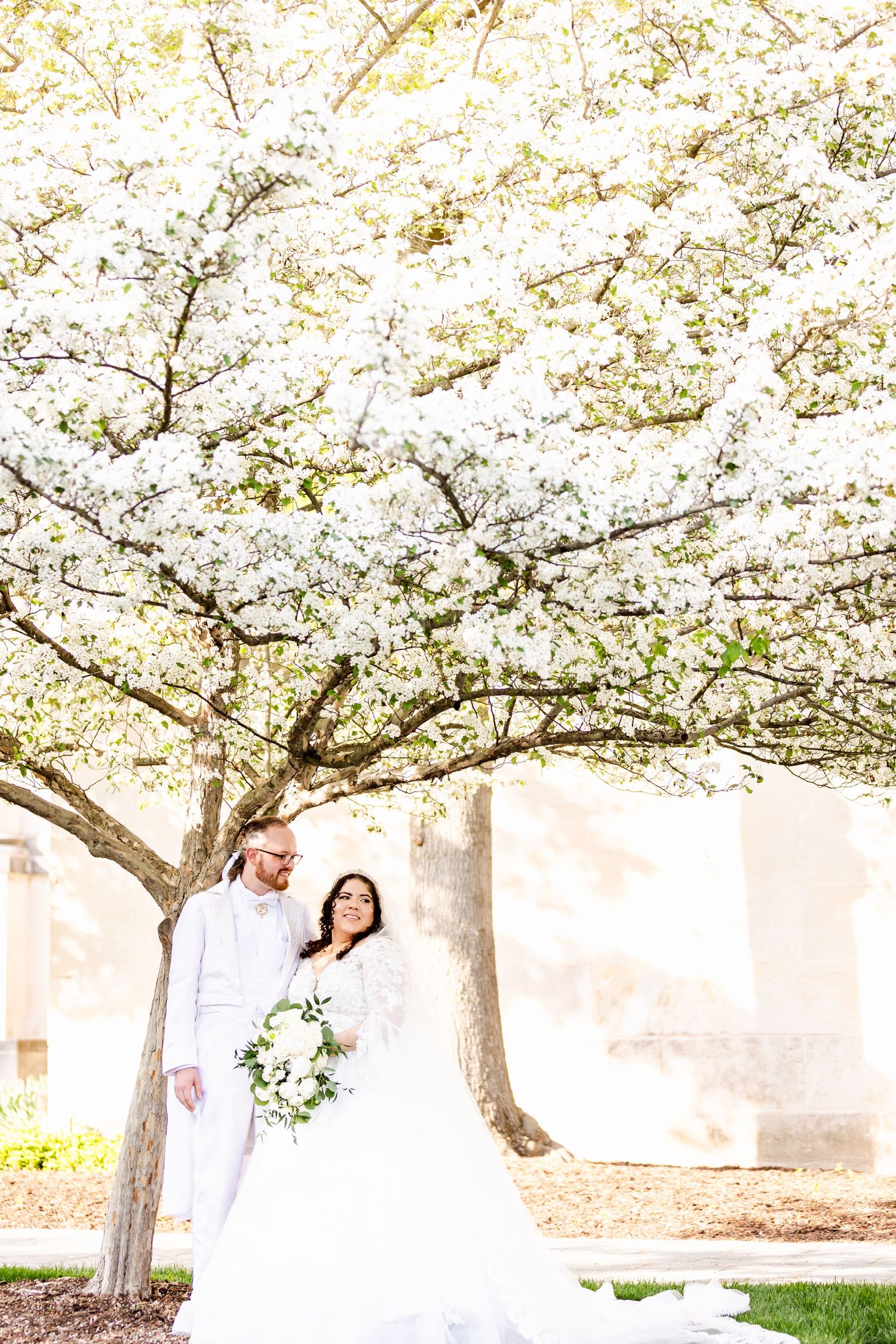 Wedding couple stands beneath blooming cherry blossom tree during spring ceremony.