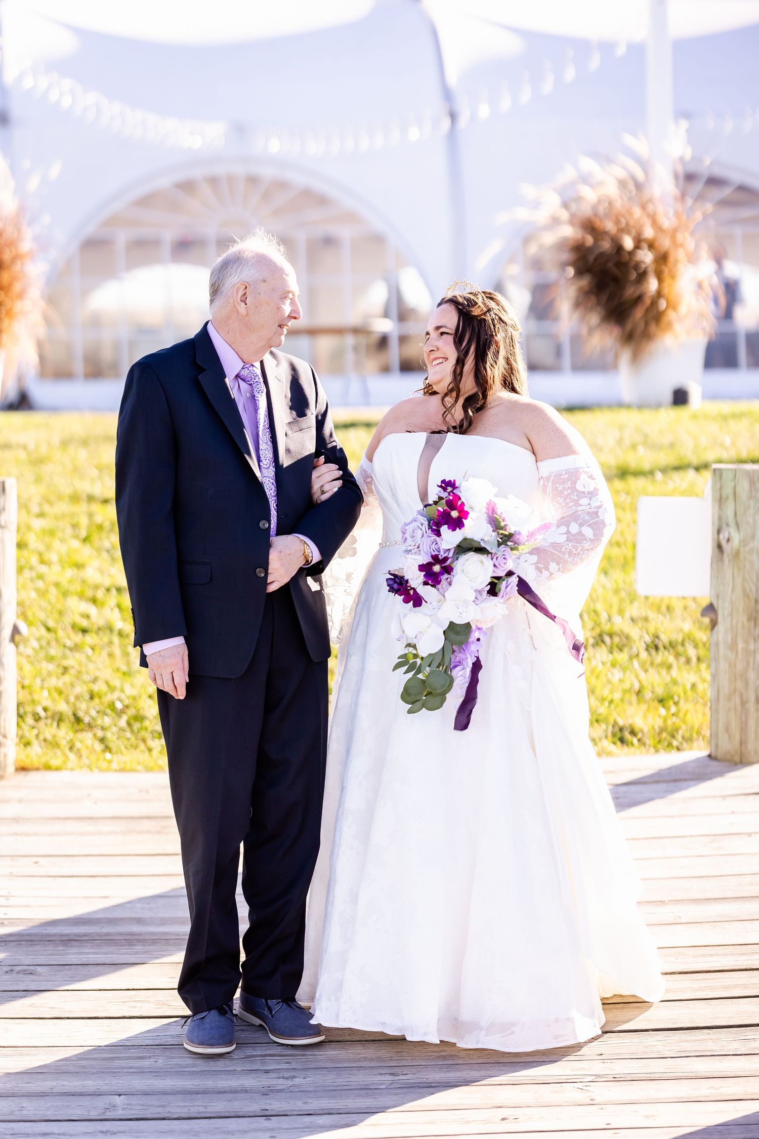 Wedding moment captured on wooden deck with white tent and dried pampas grass decorations.