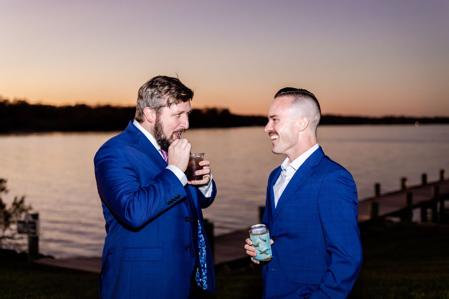 Two guests in blue suits having drinks by the waterfront at dusk.