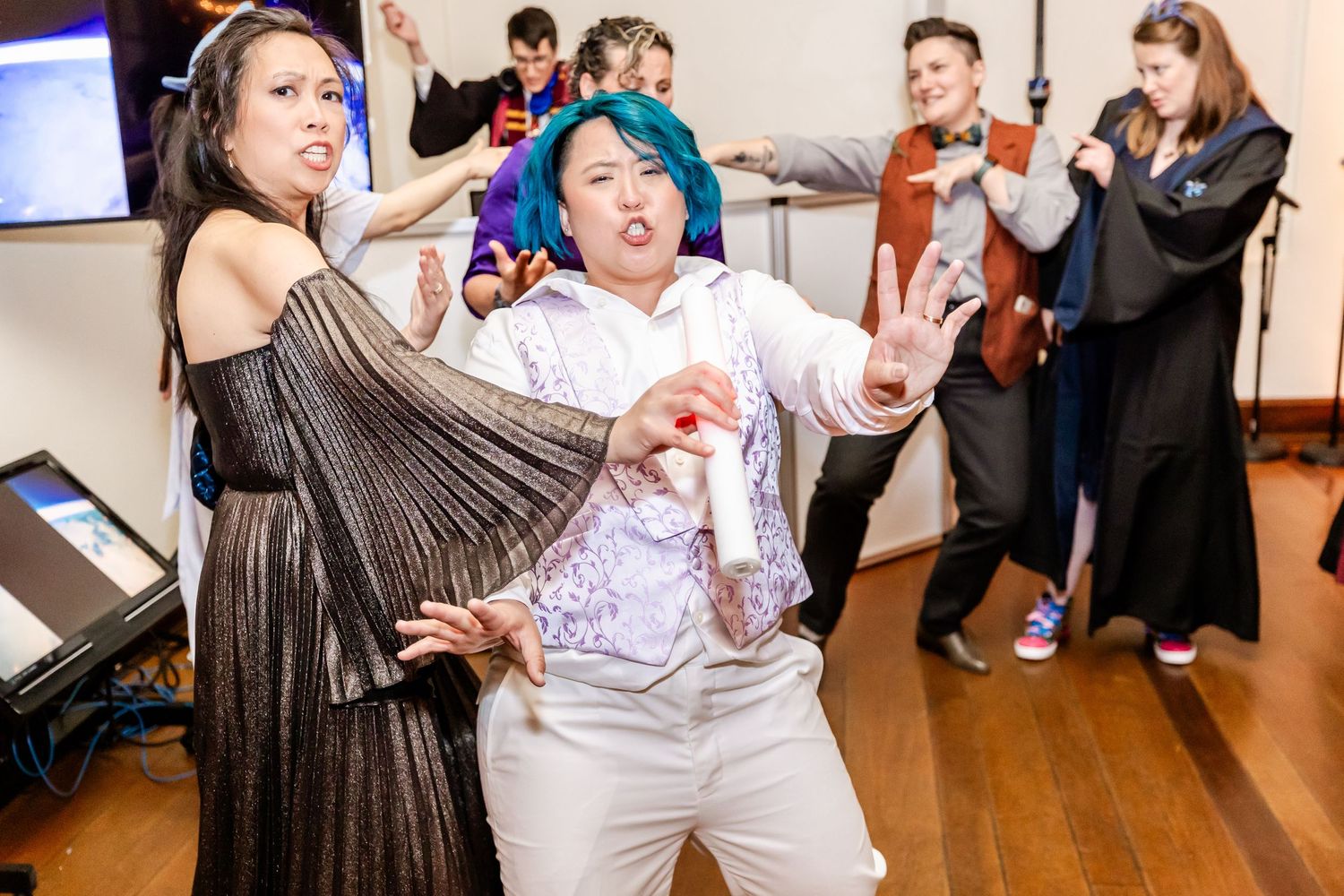 Party guests dancing together with dramatic expressions and theatrical movements on a wooden floor.