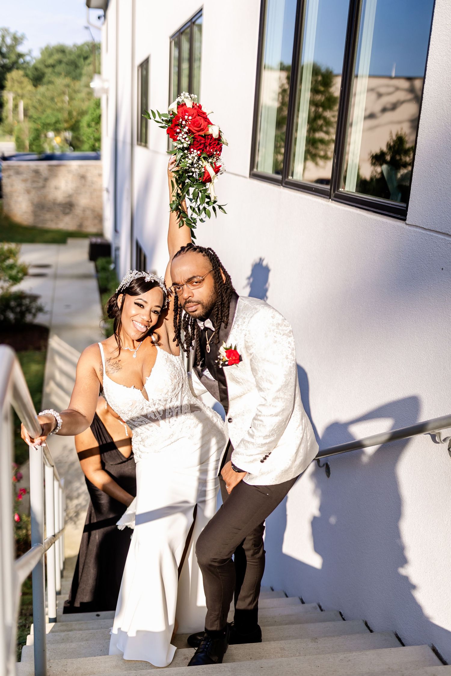 Couple sharing playful moment on white staircase with red rose bouquet.