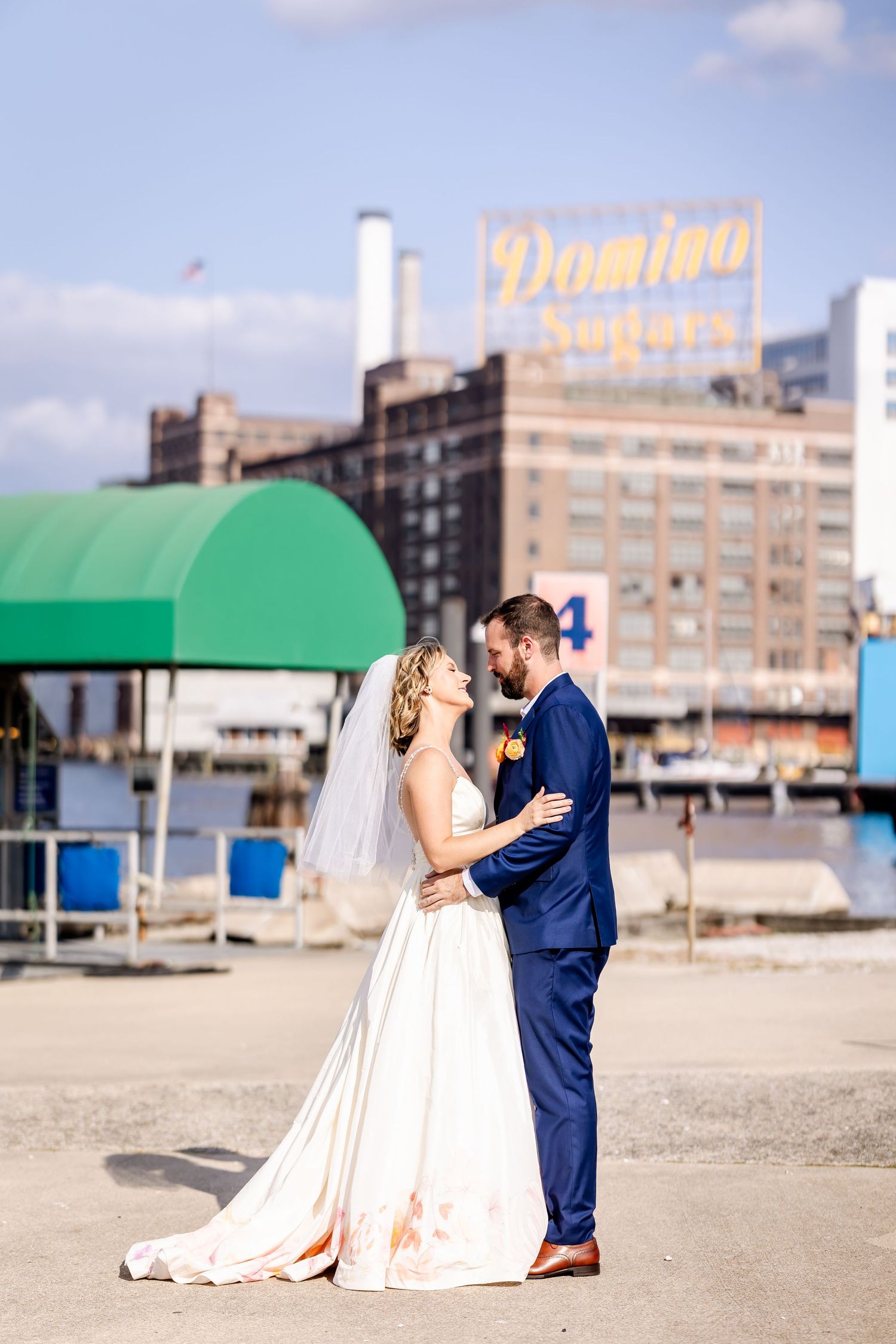 A romantic wedding portrait at a waterfront with Domino Sugar factory sign visible in background.