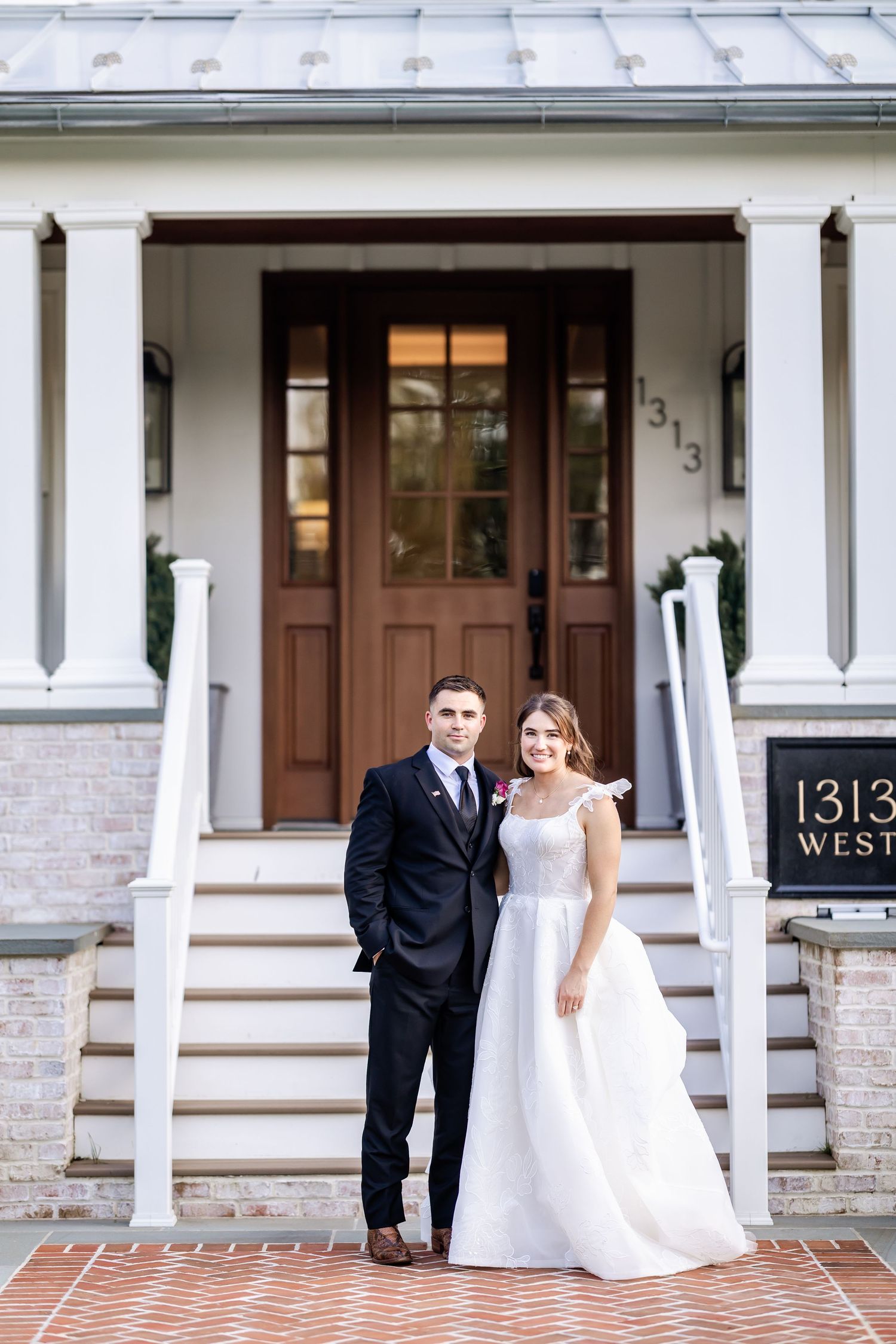 Elegant couple poses outside white columned building entrance with house number 1313.