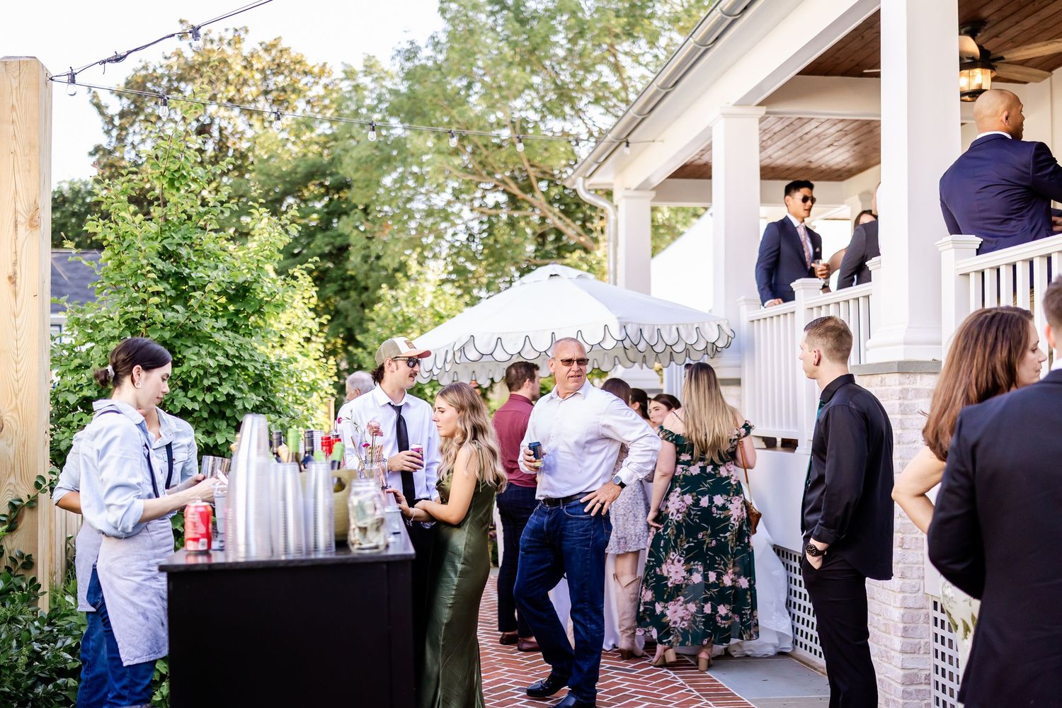 Outdoor wedding reception venue with guests mingling under wooden beams and natural lighting.