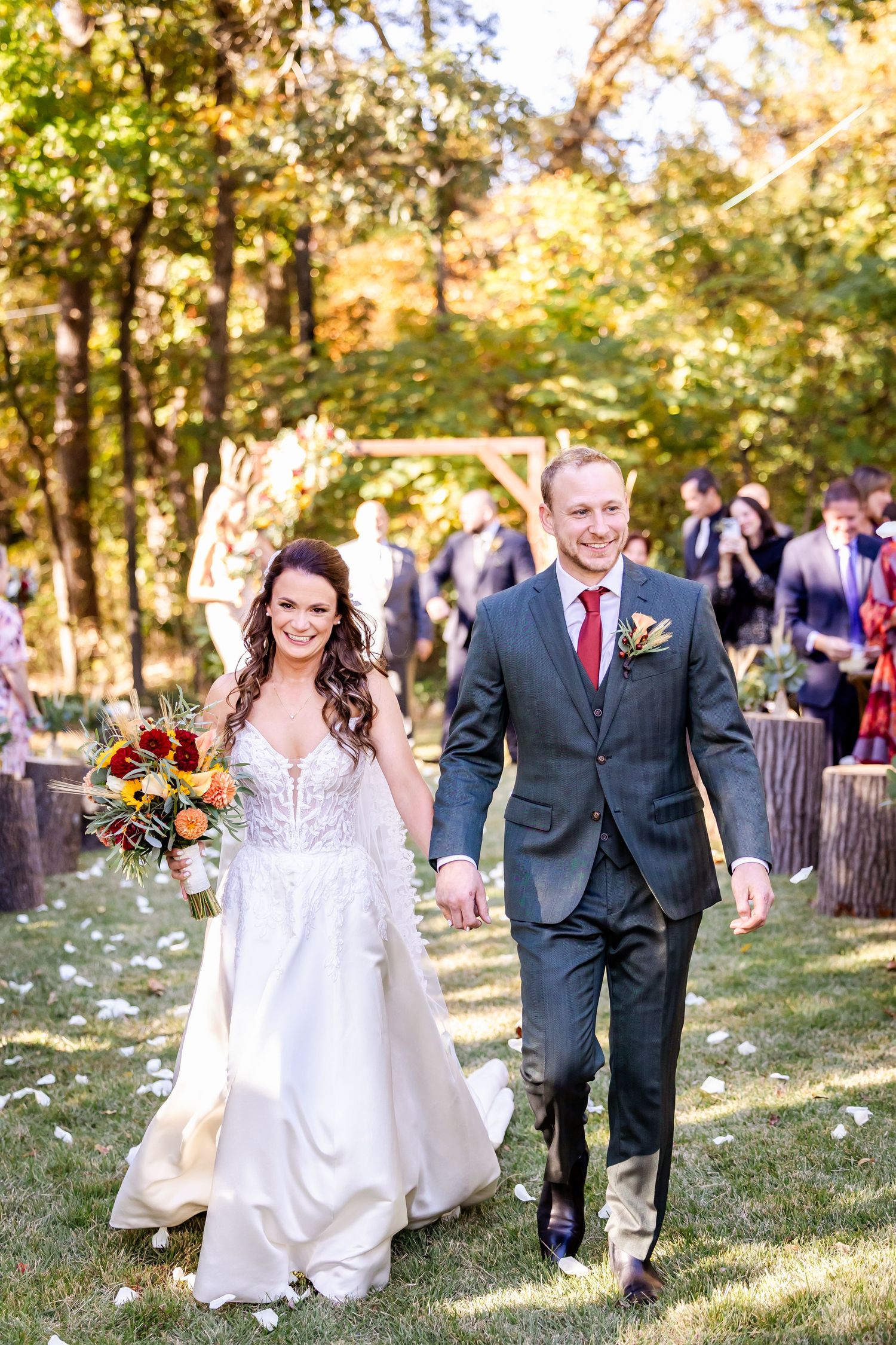 Wedding party walks joyfully across a sunny grass lawn during an autumn celebration.