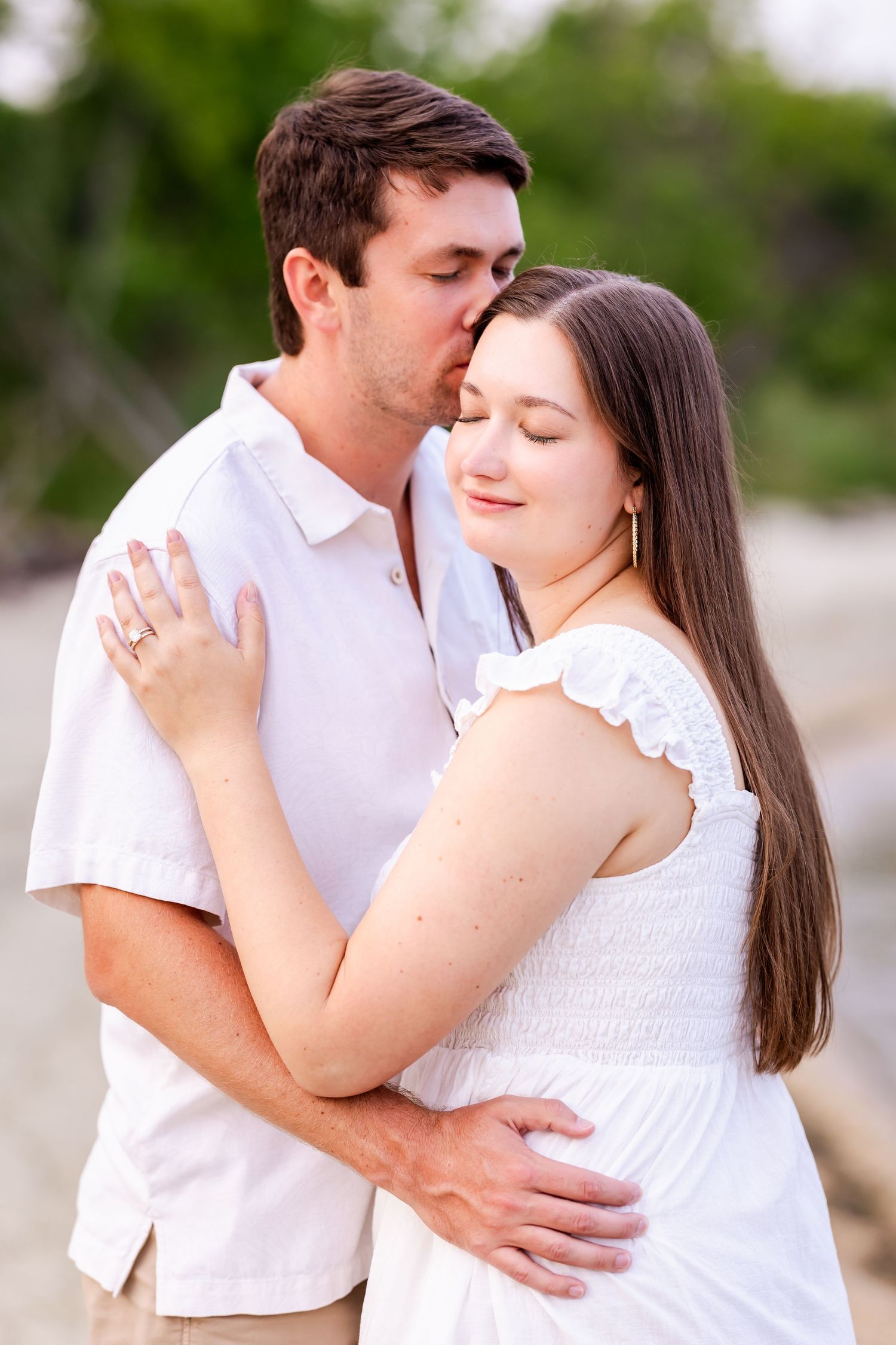 Romantic couple in white clothing embrace and share tender moments during an outdoor photoshoot in natural lighting.