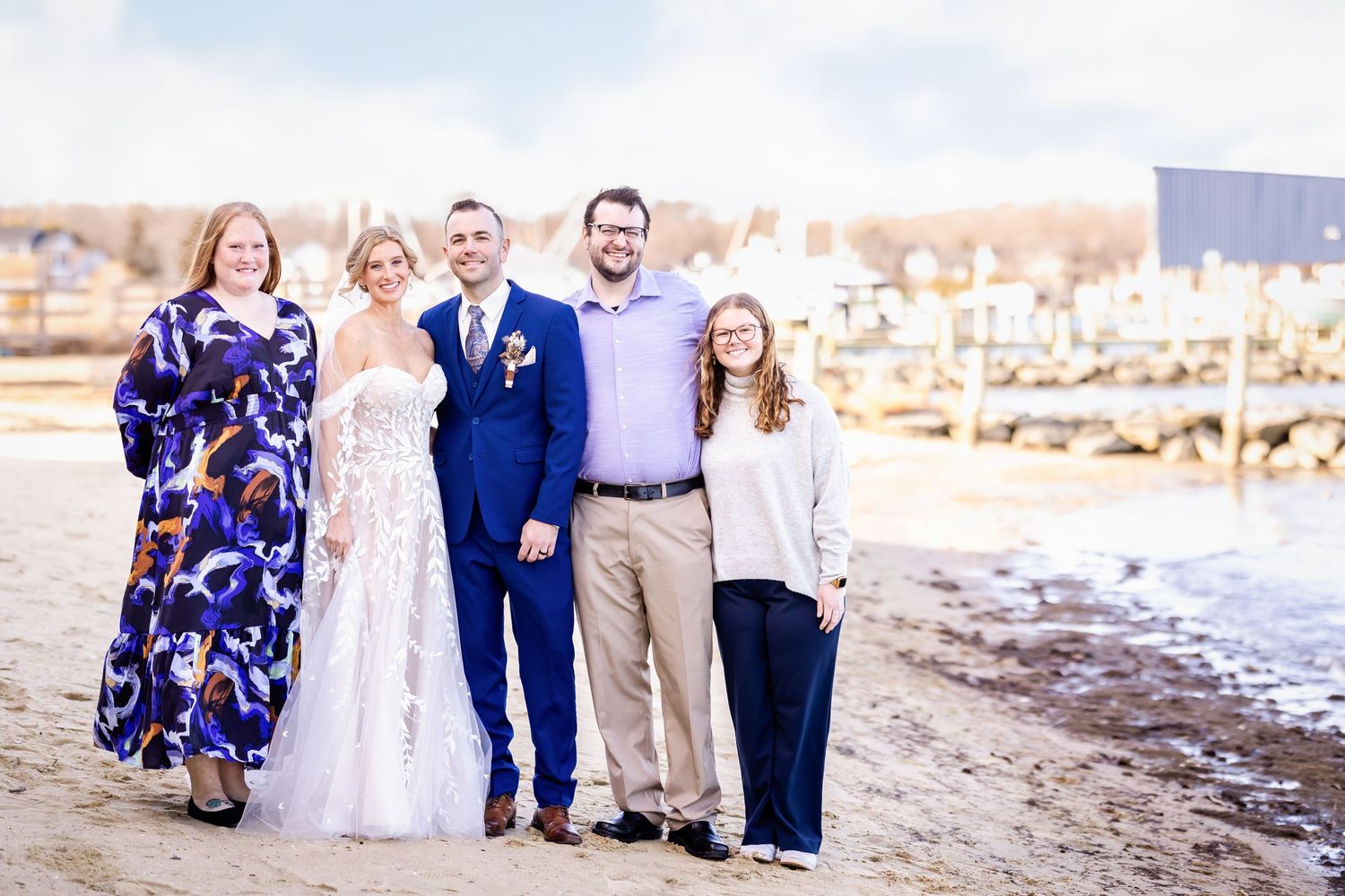 A family wedding photo taken on a sunny beach with marina in the background.