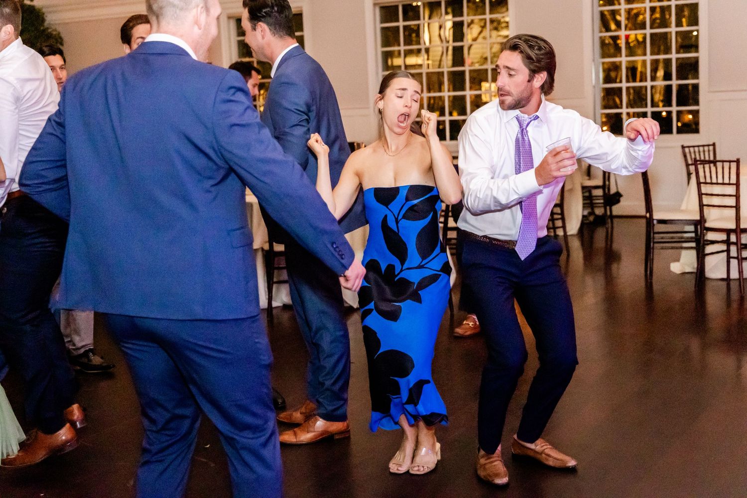 Party guests dance and celebrate on a wooden dance floor at an elegant indoor venue with formal attire.