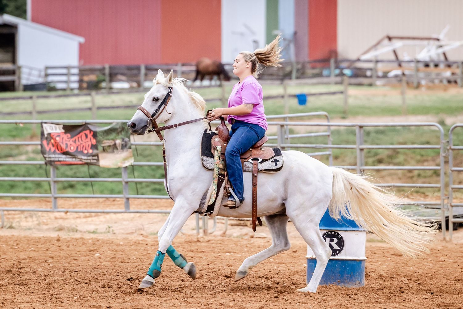 Barrel racing sequence showing horse and rider navigating around blue barrels in a sandy arena.