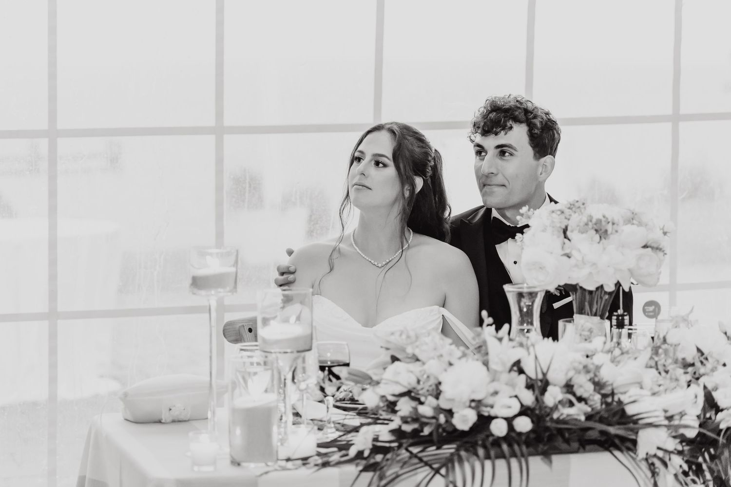 Elegant wedding reception table settings with white floral centerpieces and place cards in a bright venue.