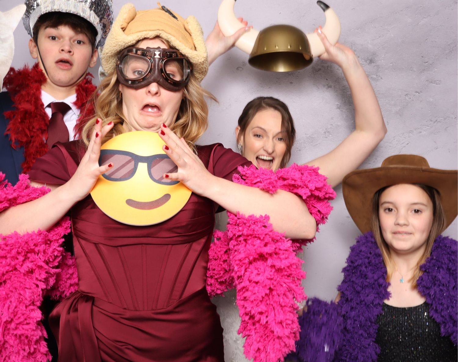 Playful photo booth scene with party guests wearing colorful boas and fun props against a grey backdrop.