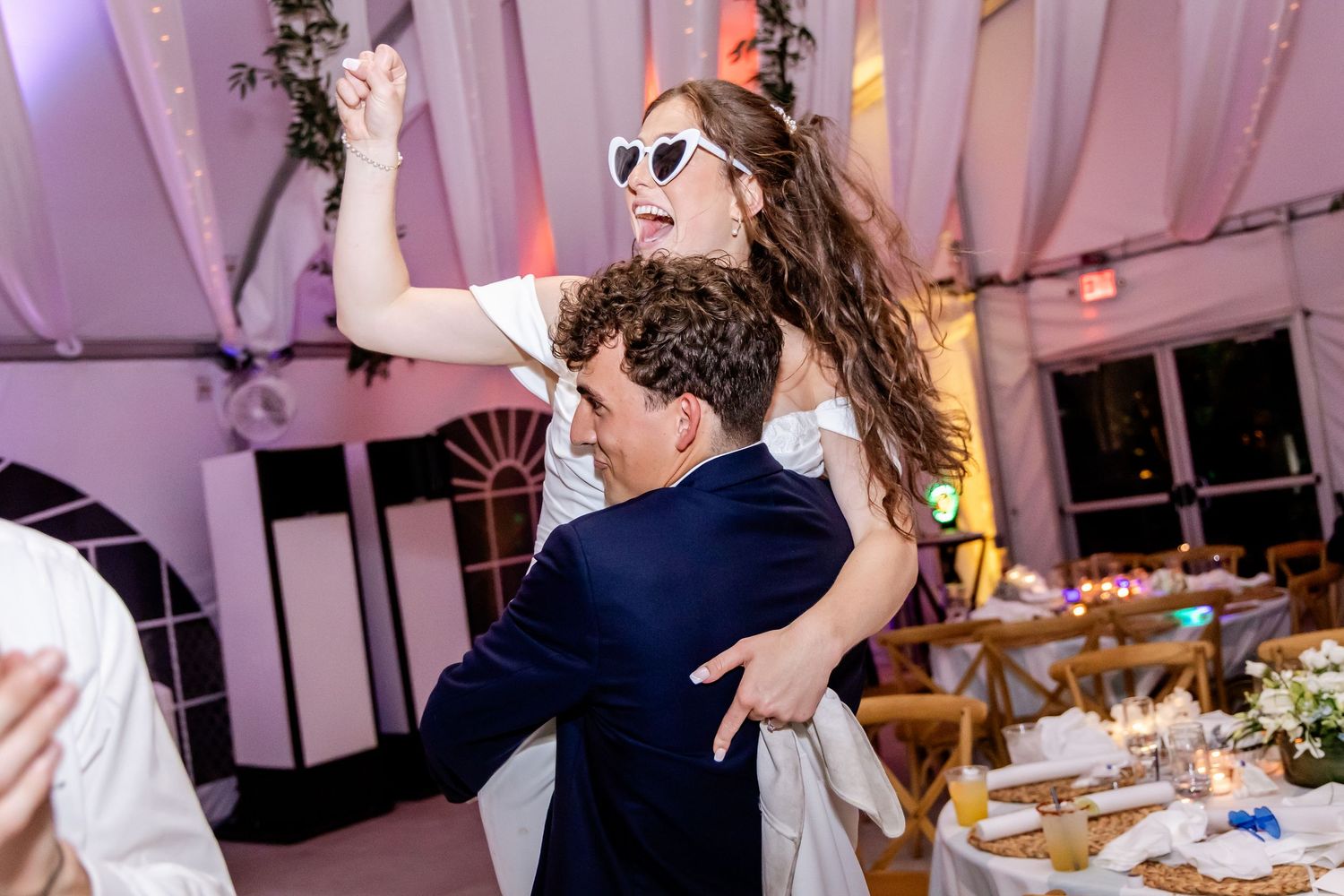 Energetic dance moves at a wedding reception with guests celebrating under draped ceiling decor.