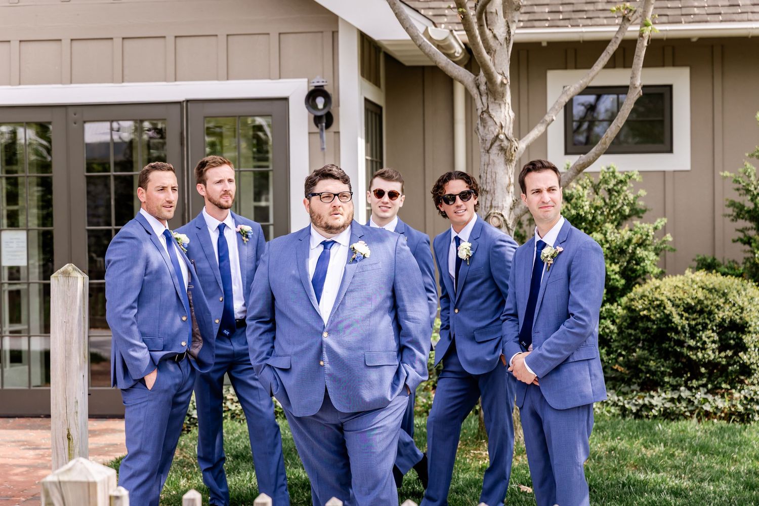 Group wearing matching blue suits pose together outside a residential building.