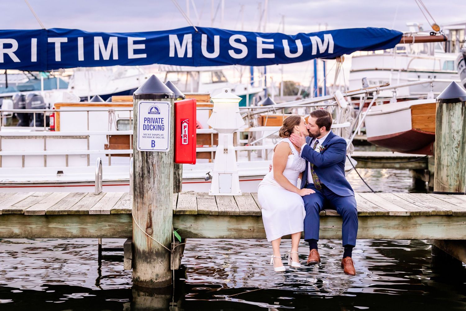 Couple sharing a romantic kiss on a dock at the Maritime Museum with boats in the background.